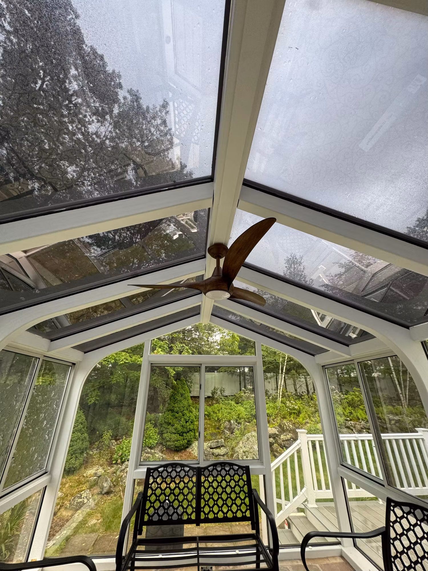 Gabled sunroom with solar control film on the glass roof and surrounding glass walls above patio seating.