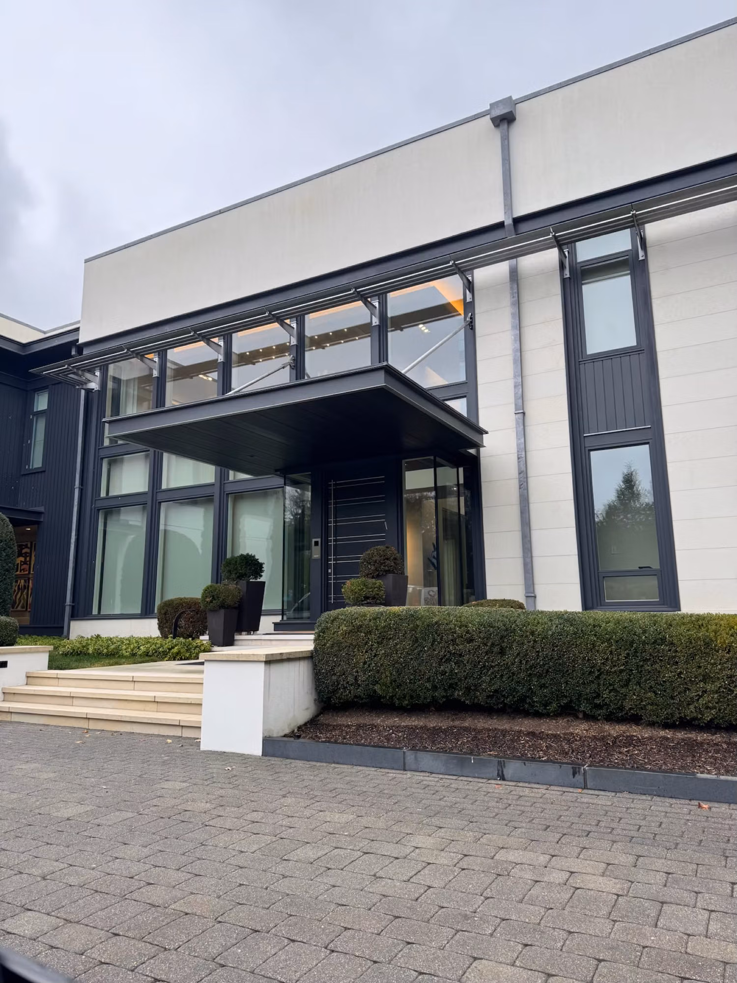 Front entry of a modern home with tall floor-to-ceiling glass panels and an upper window band over the covered portico.