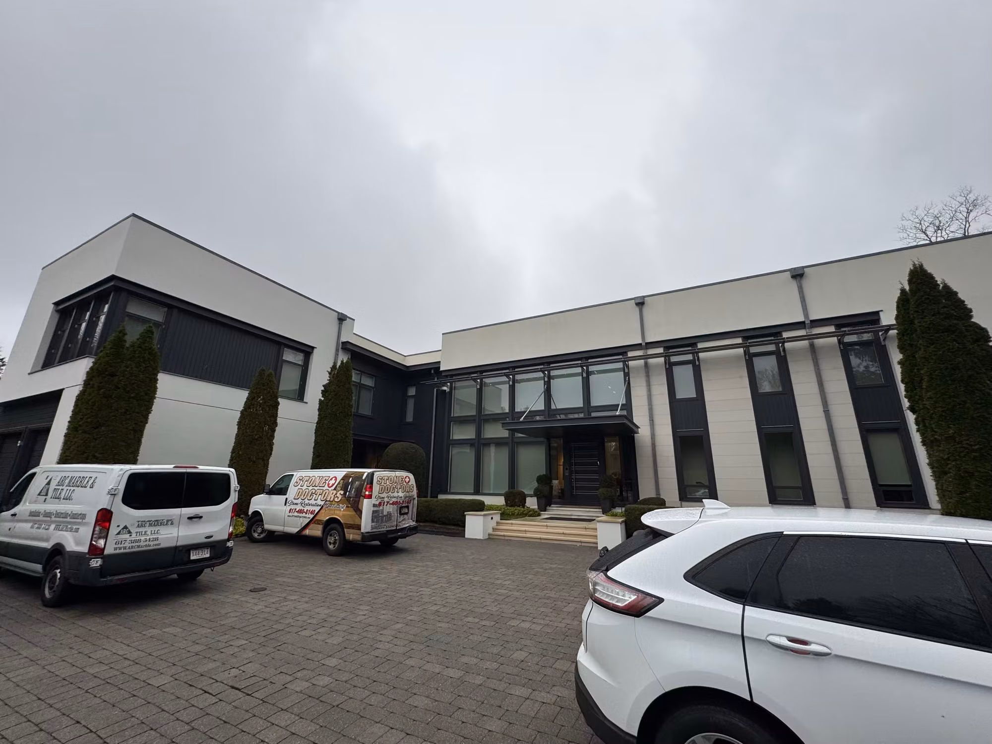 Work vans parked outside a modern two-story home with large dark-framed windows during a residential window film install.