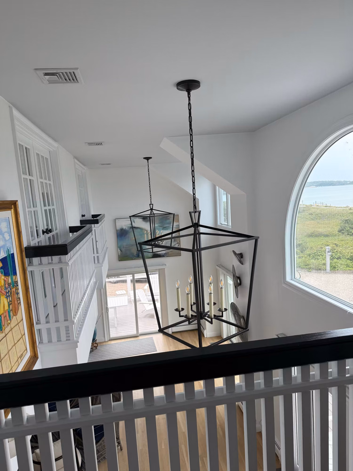 Tall arched landing window with a coastal view, fitted with clear residential window film over the stair railing.