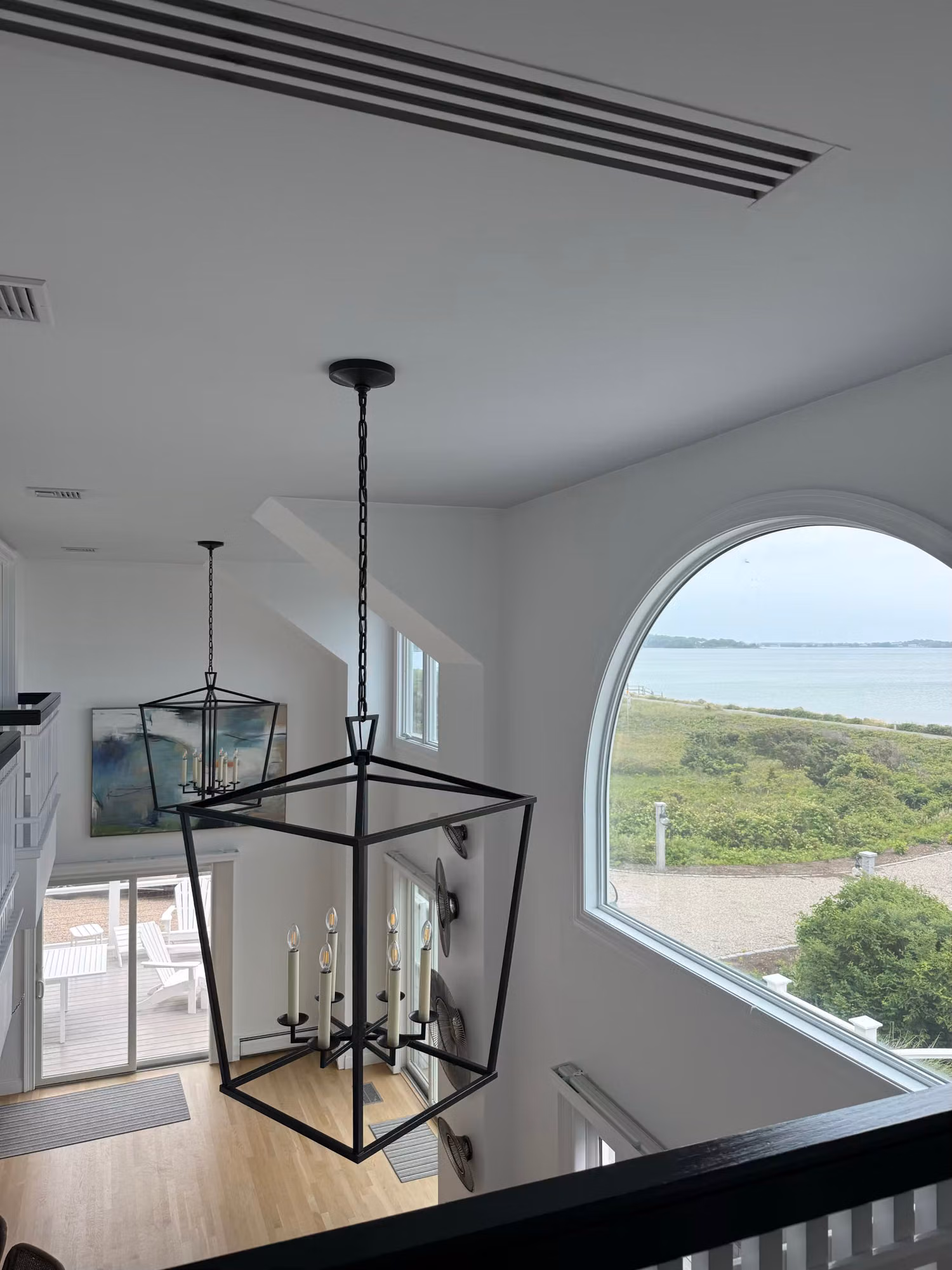 Large arched loft window overlooking the bay with clear window film protecting the open living space below.