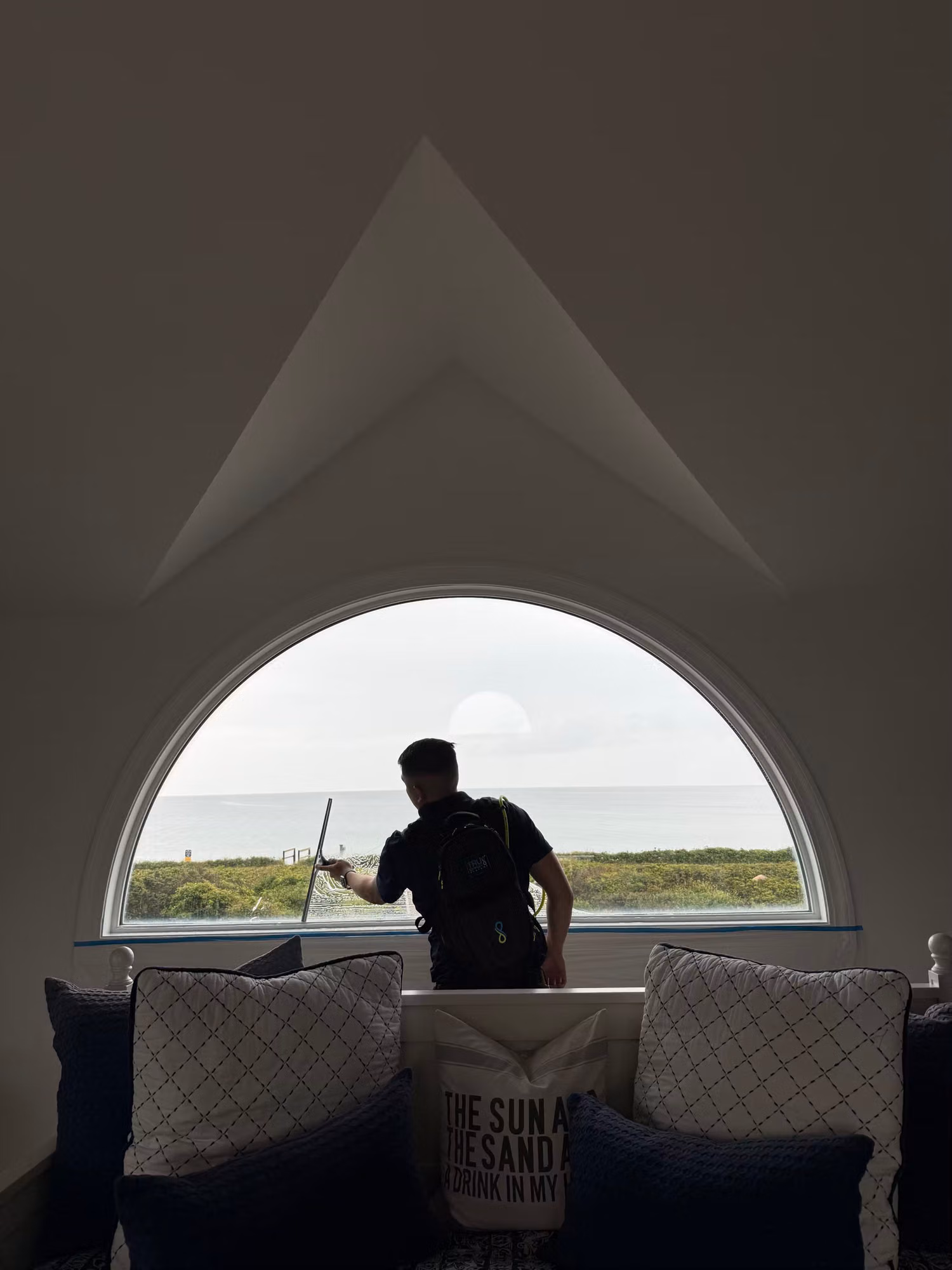 Installer squeegees window film onto a large half-round arched bedroom window overlooking the ocean.