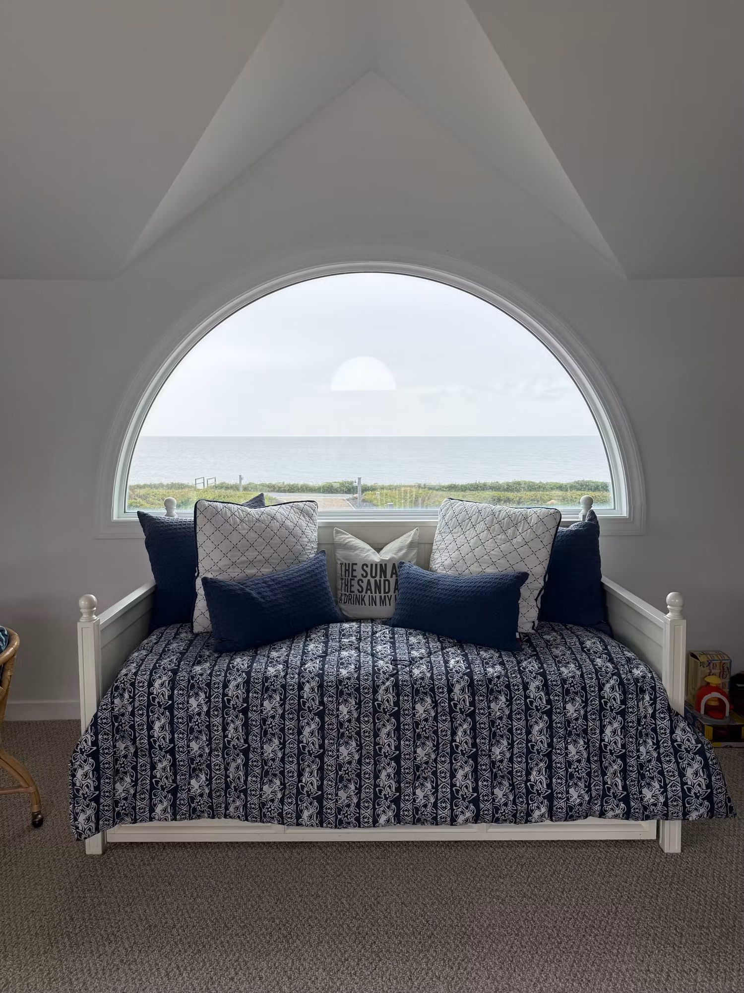 Daybed set beneath a large arched bedroom window with an ocean view through treated glass.