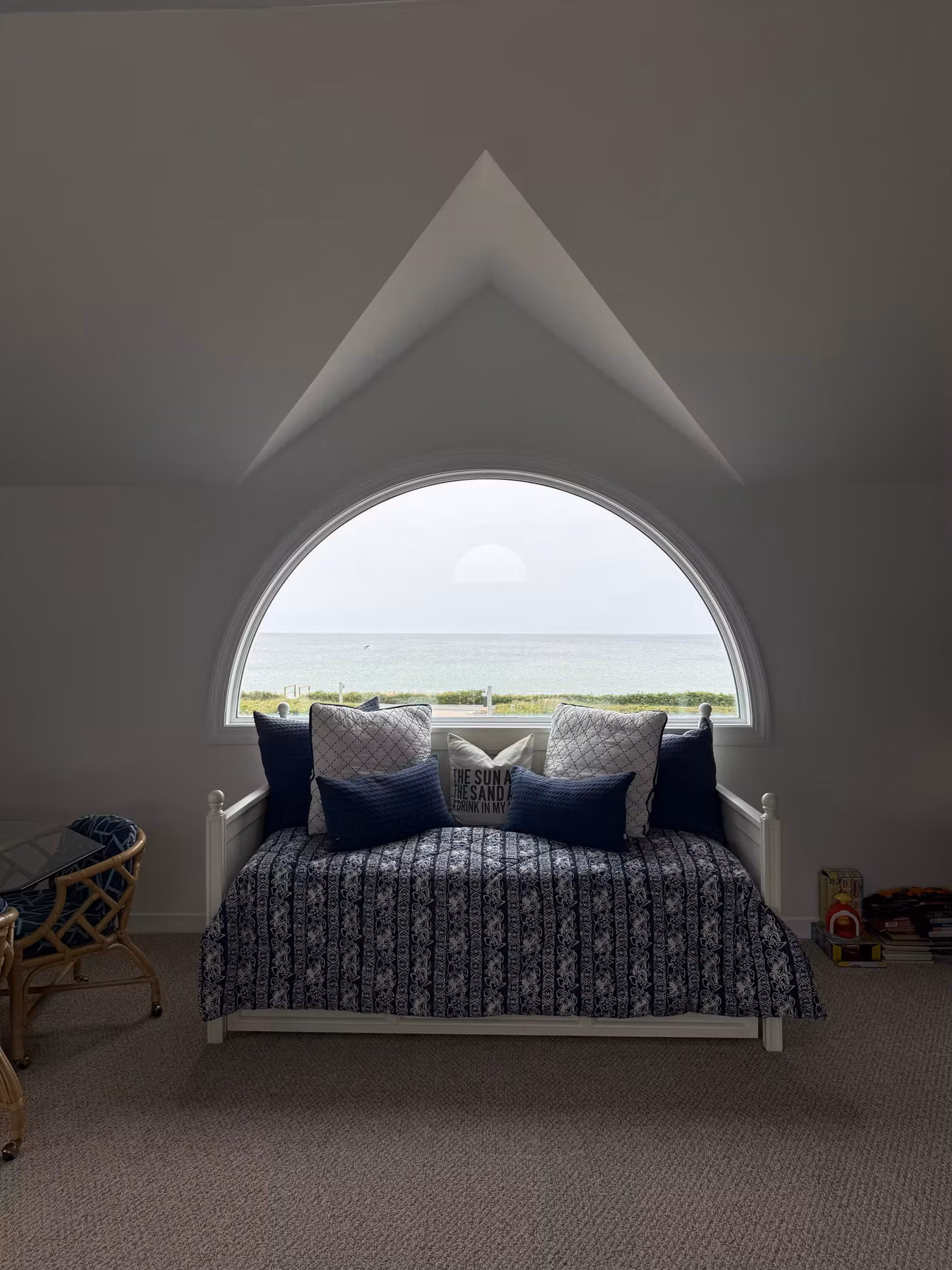 Bedroom reading nook with an arched picture window and daybed framing an ocean view through clear window film.