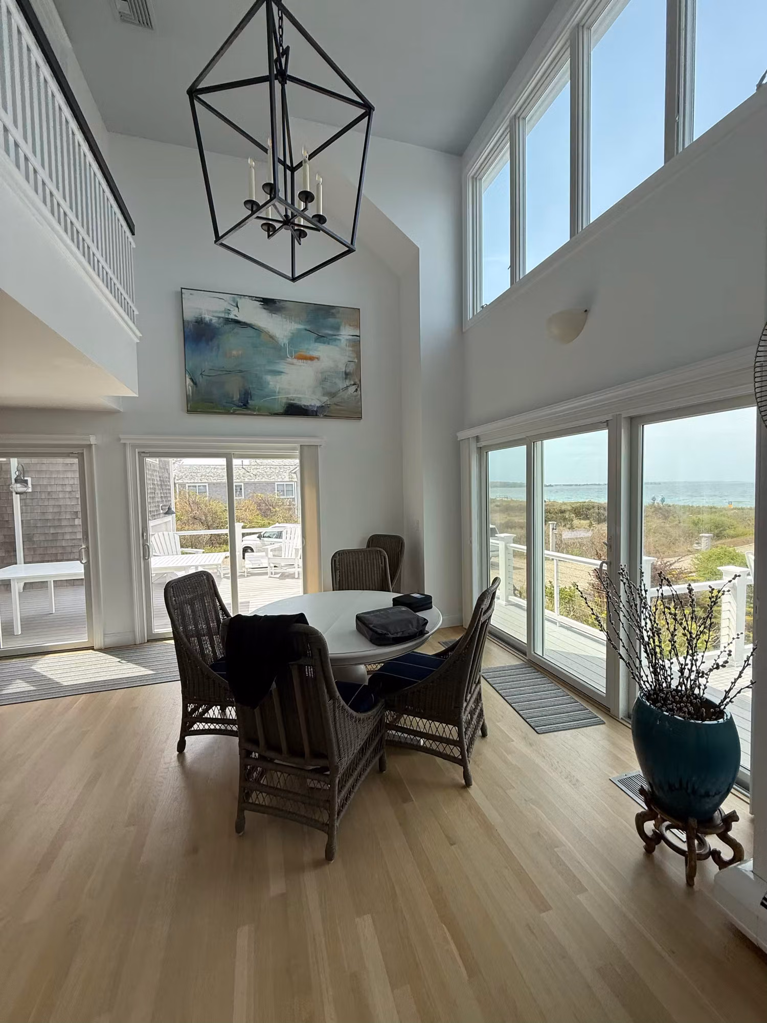 Floor-to-ceiling dining room windows and glass slider with clear film framing an ocean view in a coastal home.