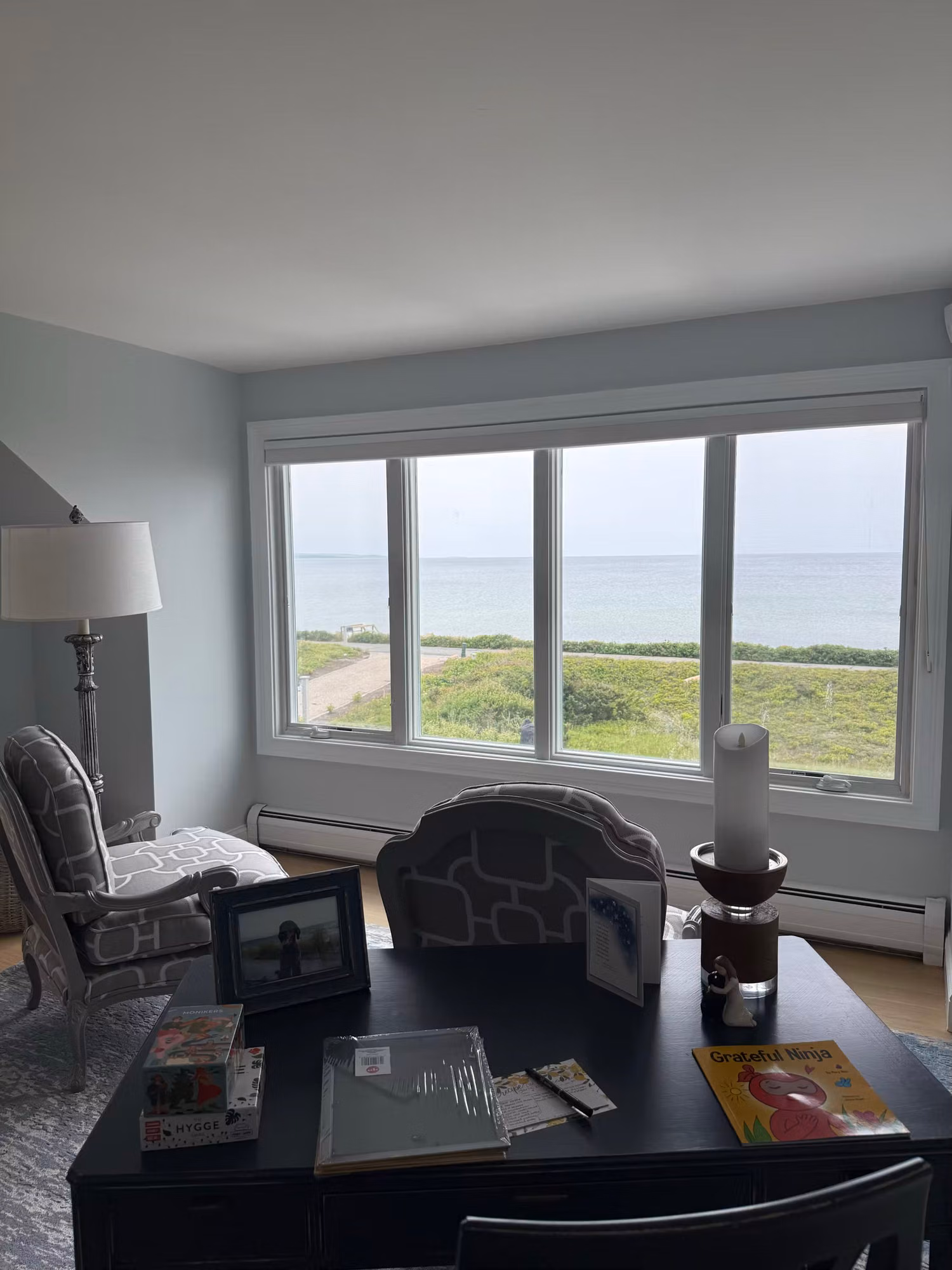 Home office with a large picture window treated with clear film overlooking a coastal shoreline.
