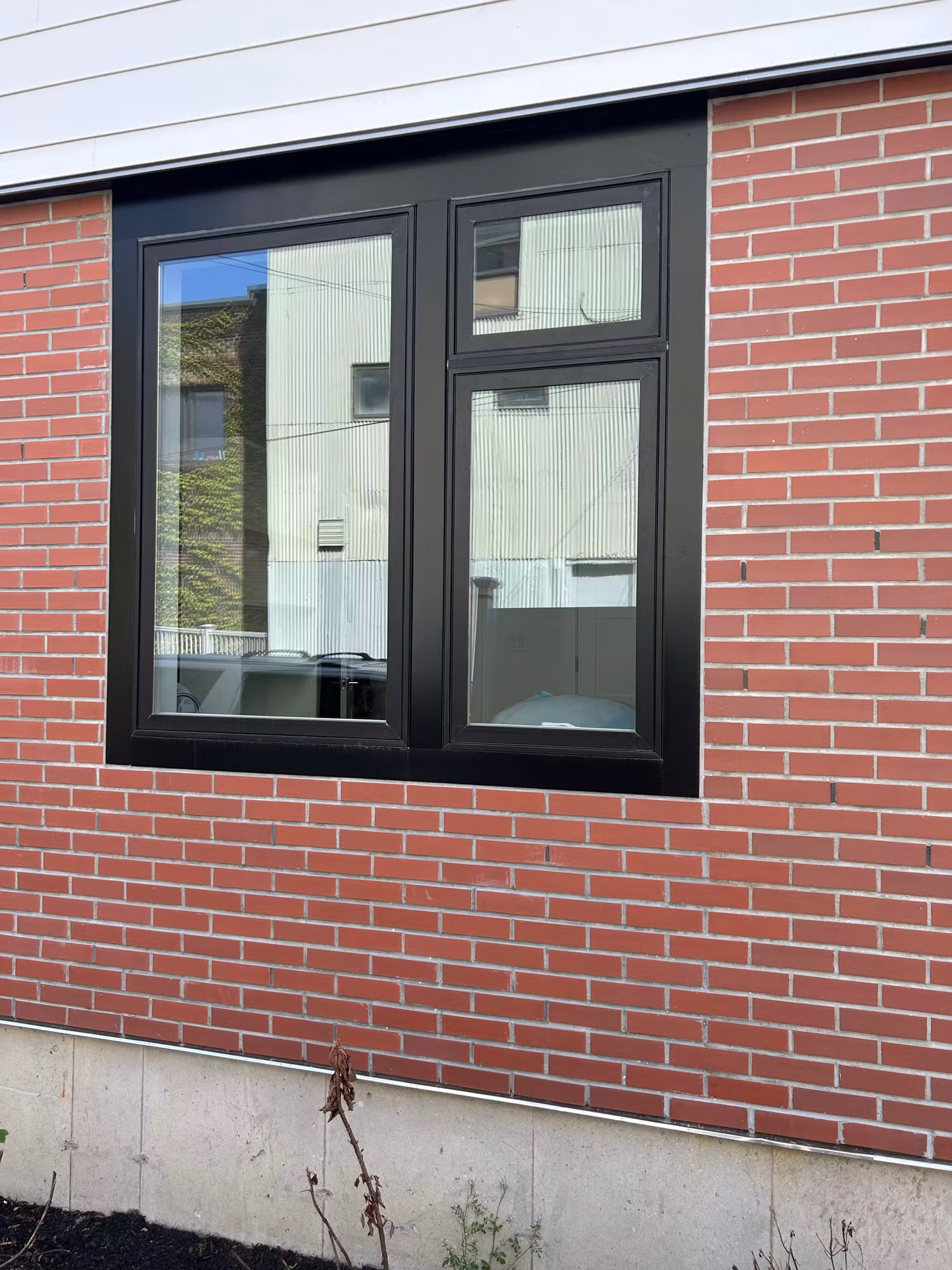 Black-framed sliding window set in a red brick wall with clear reflective glass on a residential exterior.