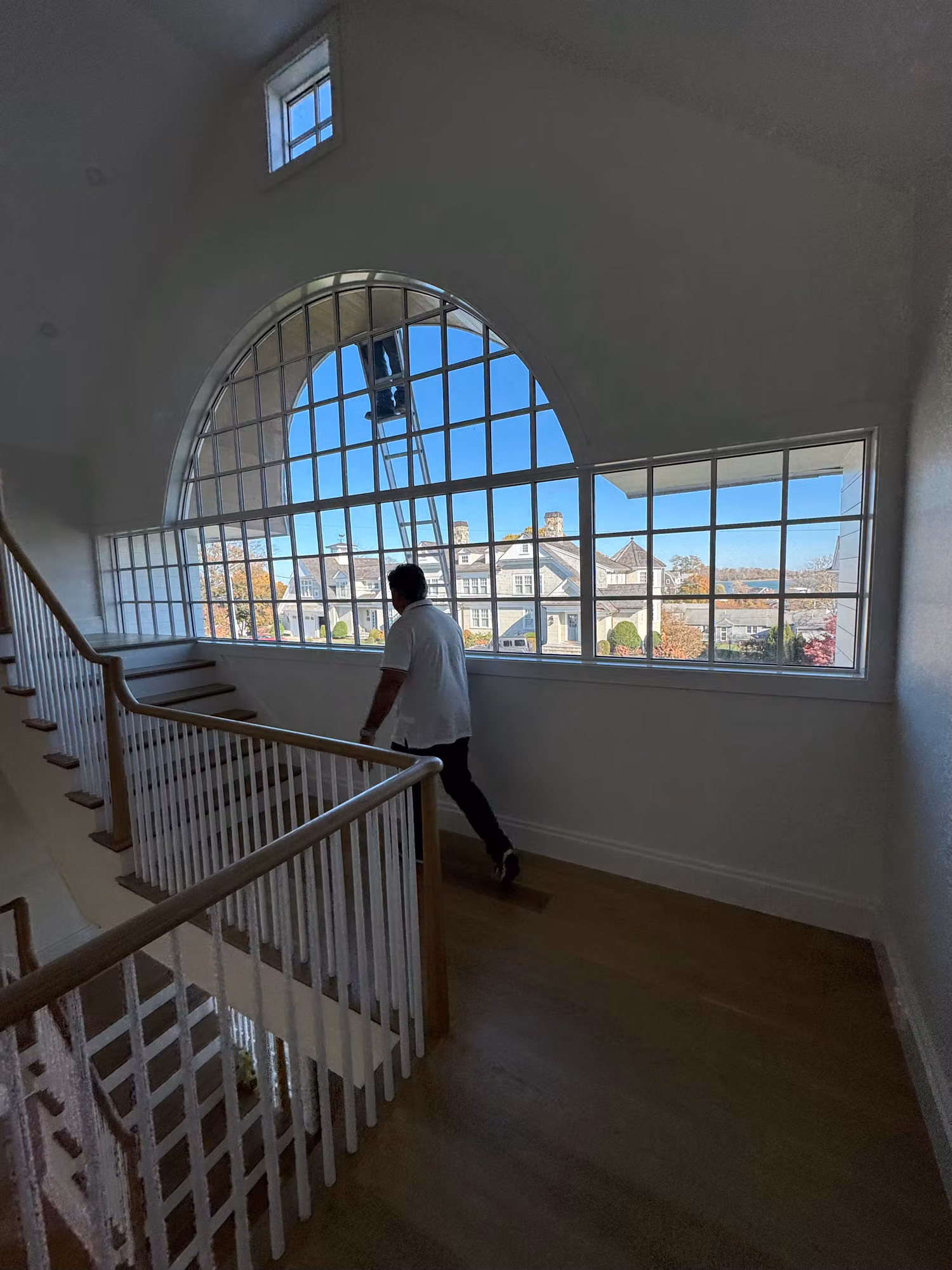 Large arched divided-light stairwell window with an installer and ladder during a residential window film job.