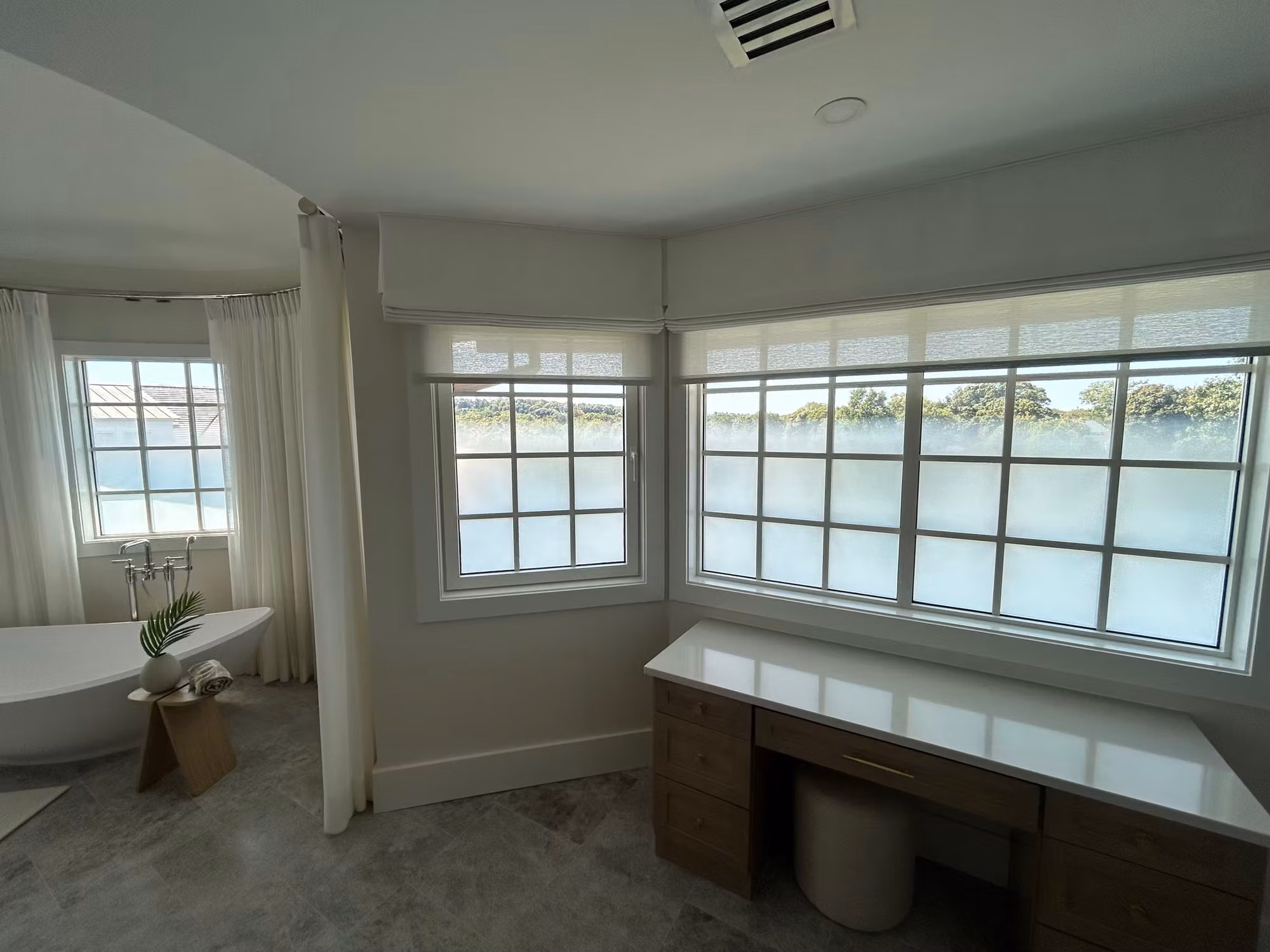 Bathroom corner with freestanding tub and divided-light windows showing frosted privacy film across the lower panes.