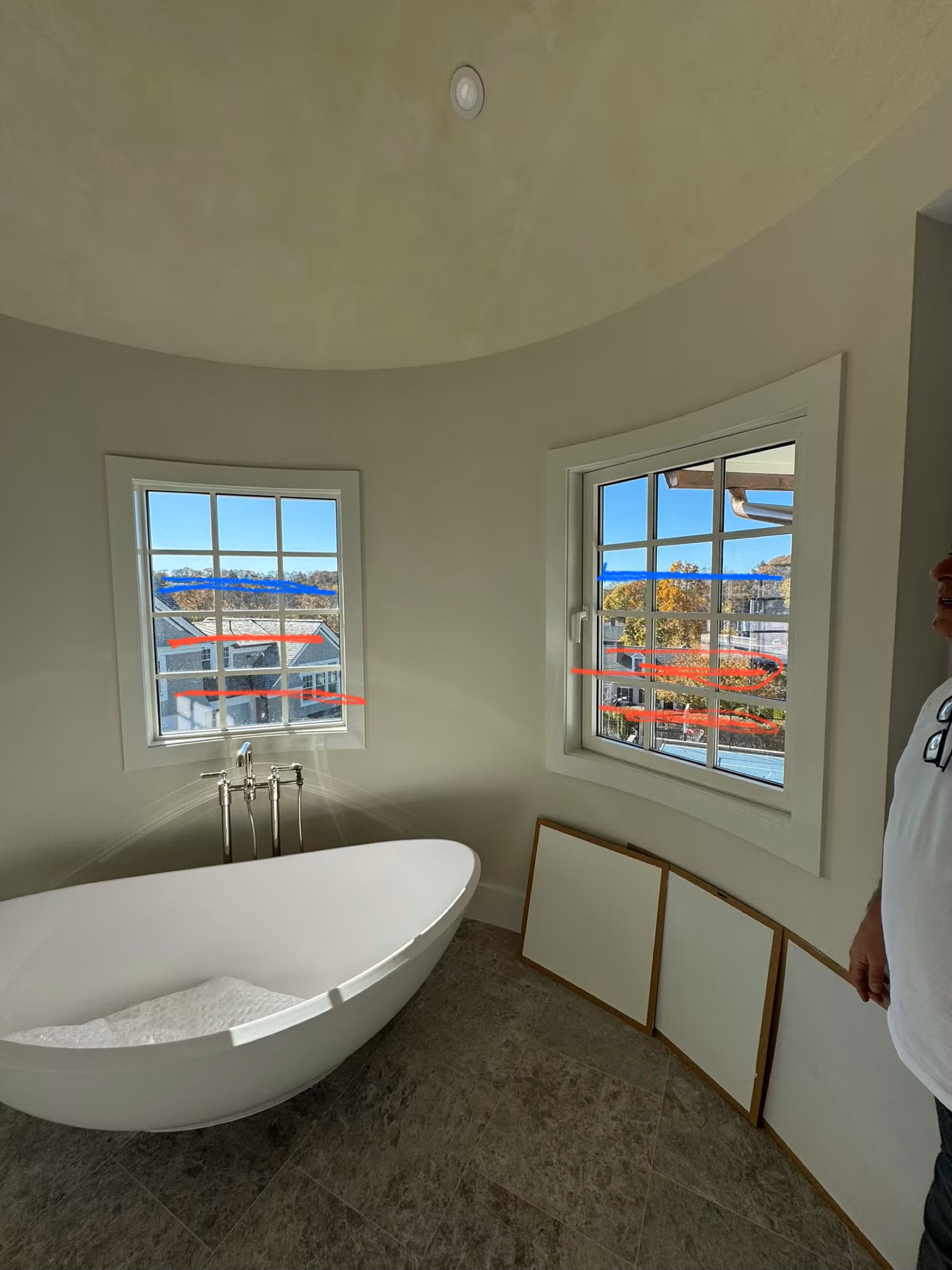 Freestanding tub beside two divided-light windows with red prep tape marking the glass during a film installation.
