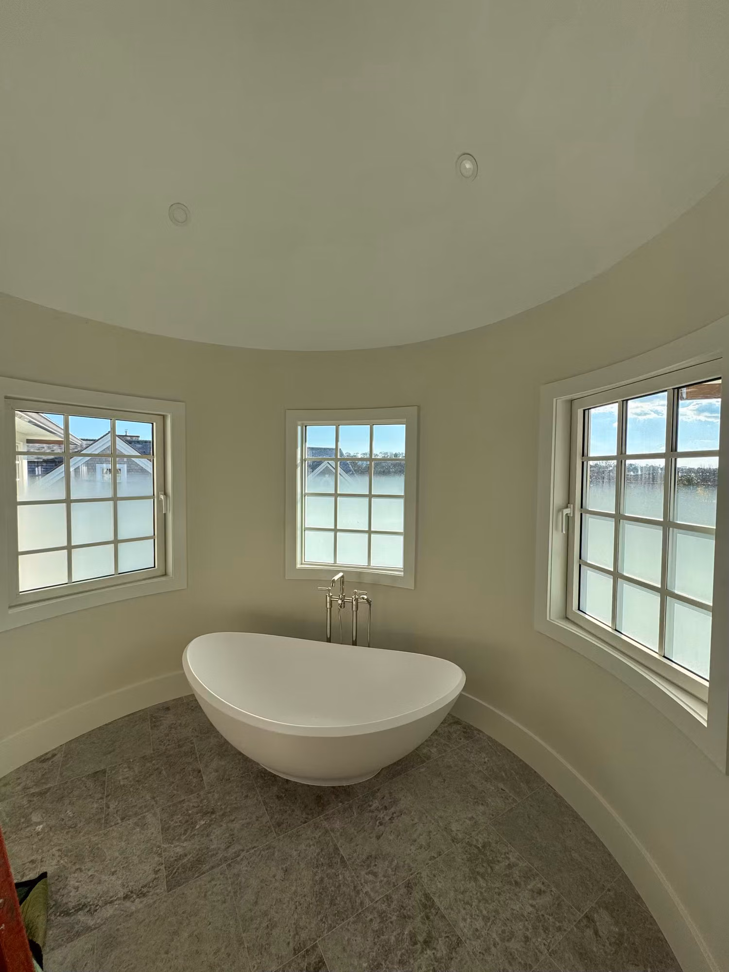 Curved bathroom wall with a freestanding soaking tub and grid windows whose lower panes have frosted privacy film.