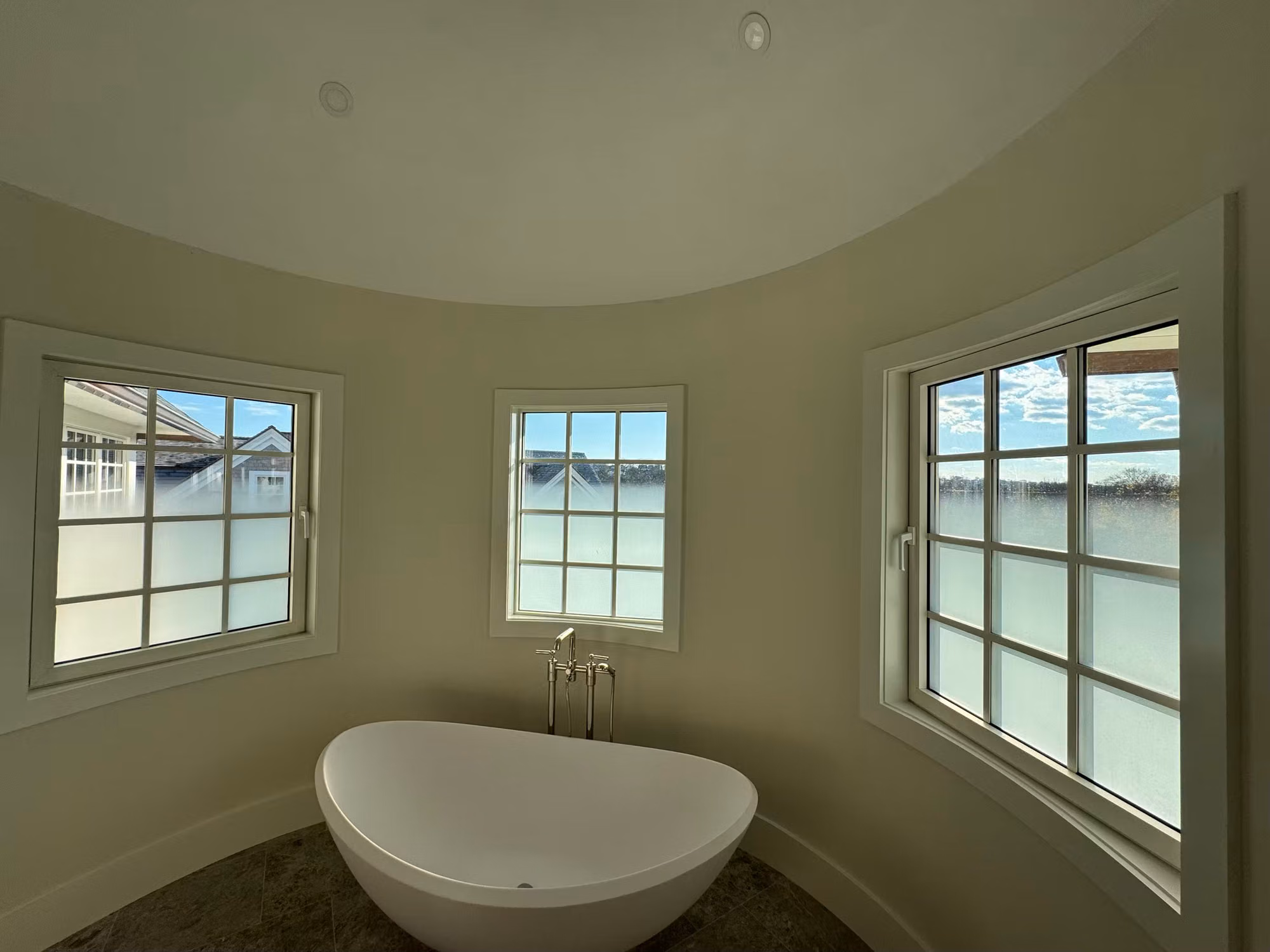 Curved bathroom with a freestanding tub and several grid windows whose lower panes carry frosted privacy film.