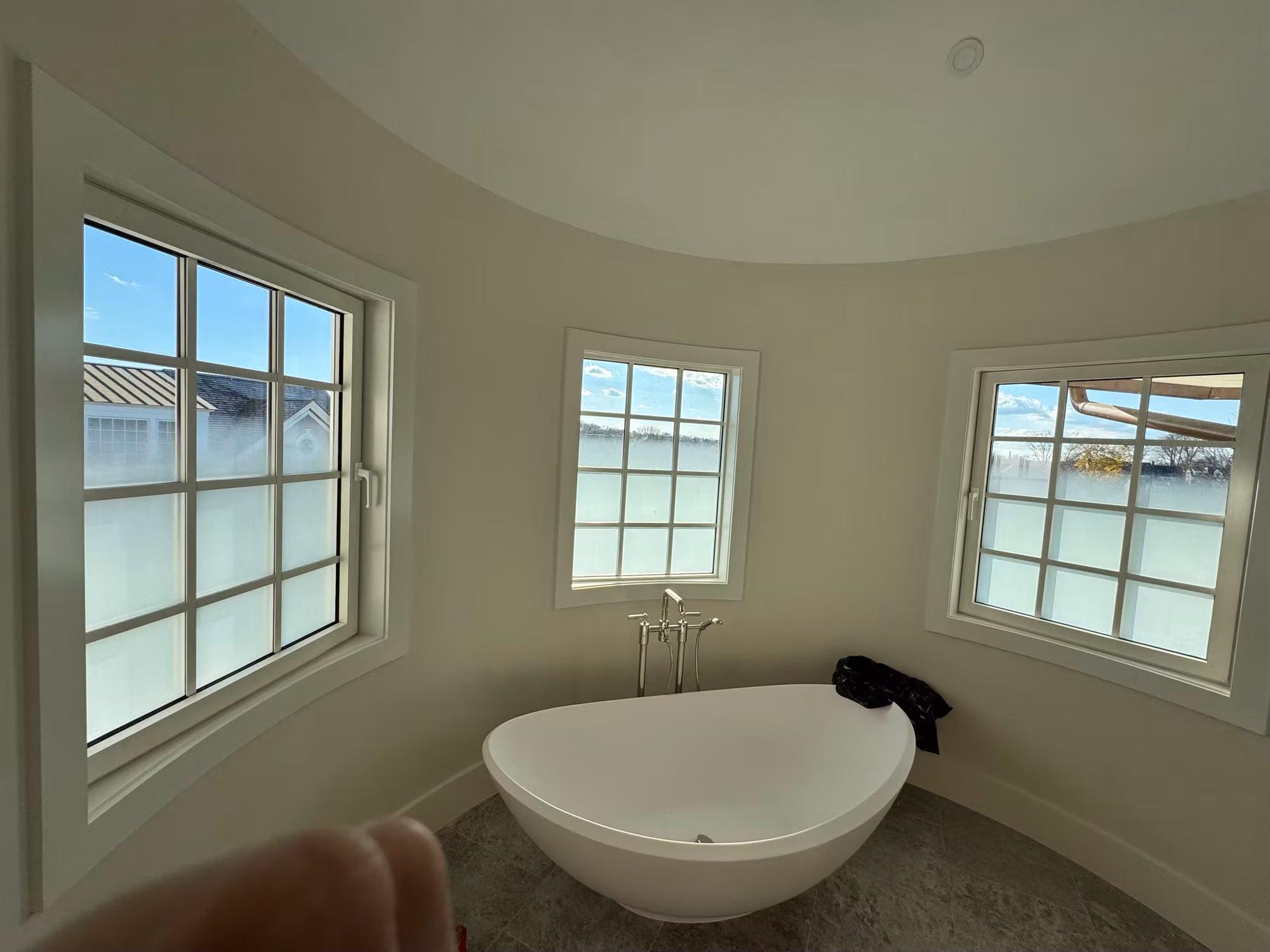 Curved bathroom turret with three divided-light windows frosted on their lower halves for privacy above a soaking tub.