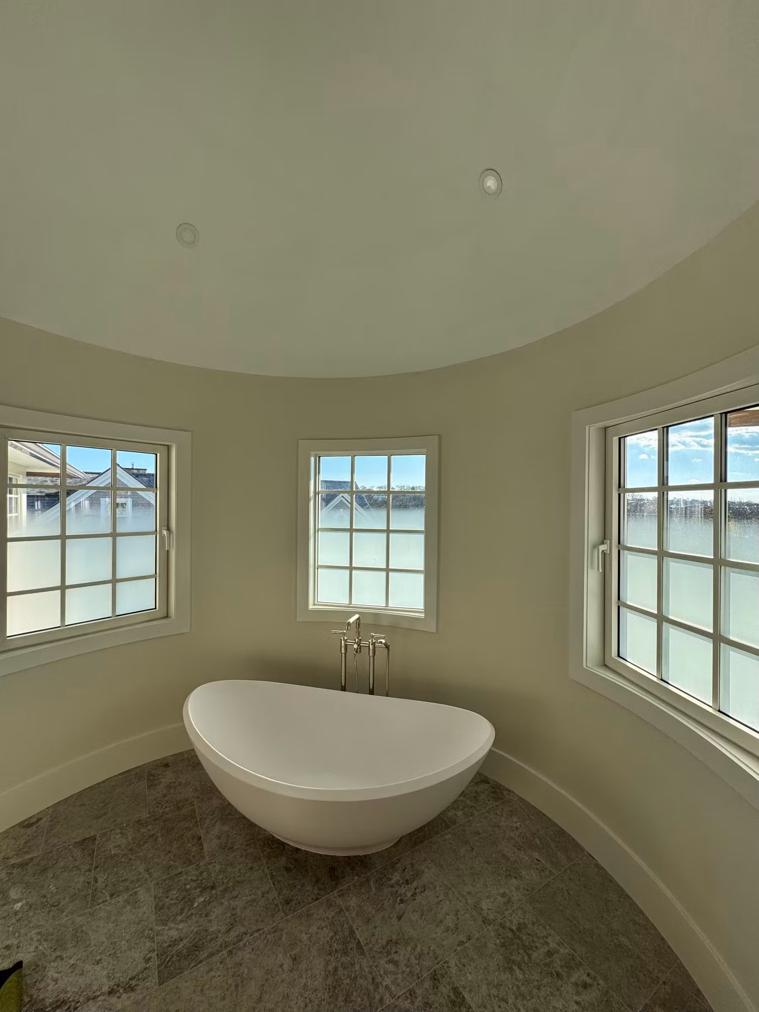 Freestanding tub set in a curved bathroom turret with frosted privacy film along the lower panes of three windows.