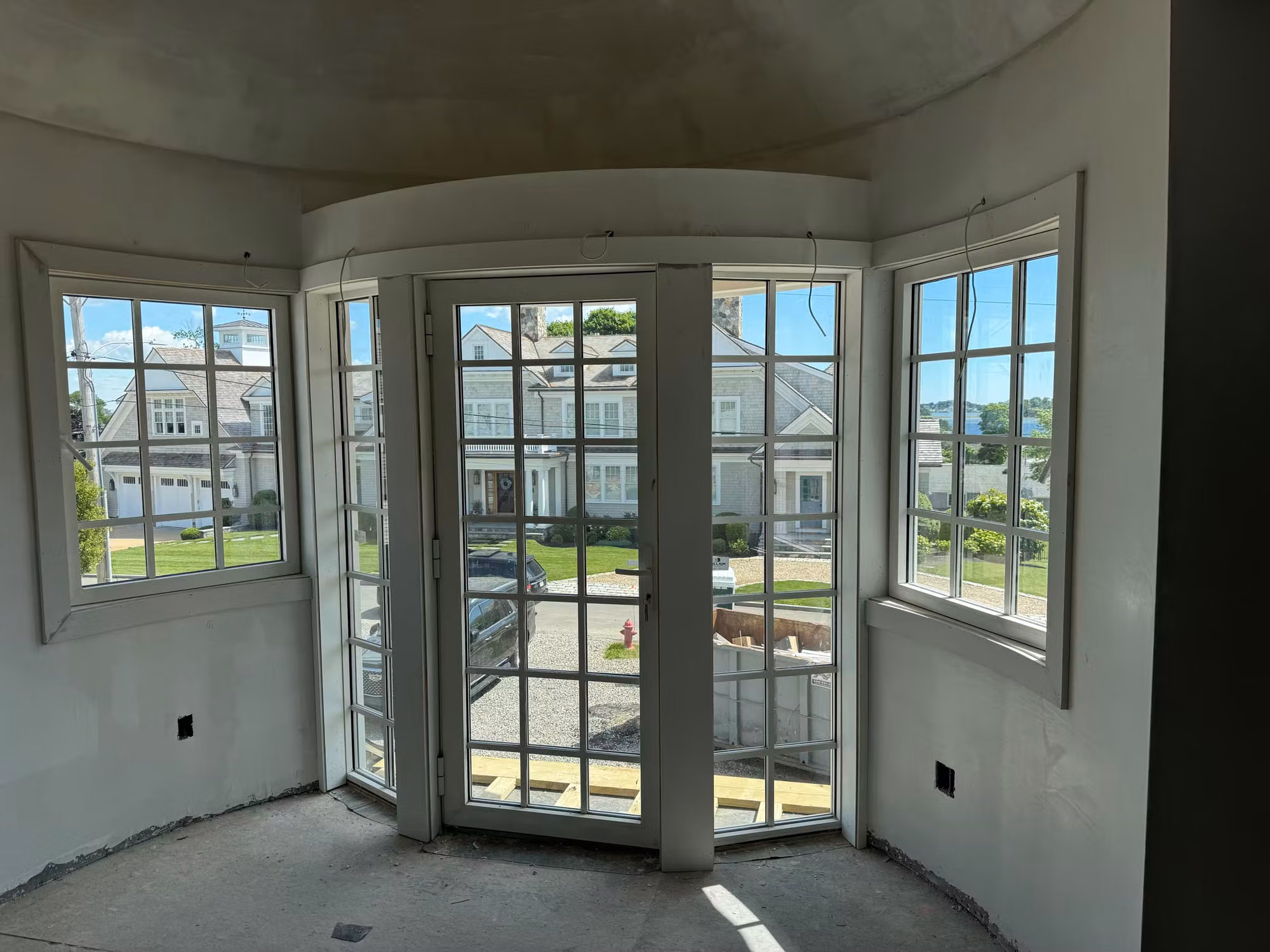 Curved bay with divided-light French doors and flanking grid windows in clear glass during a construction-stage renovation.
