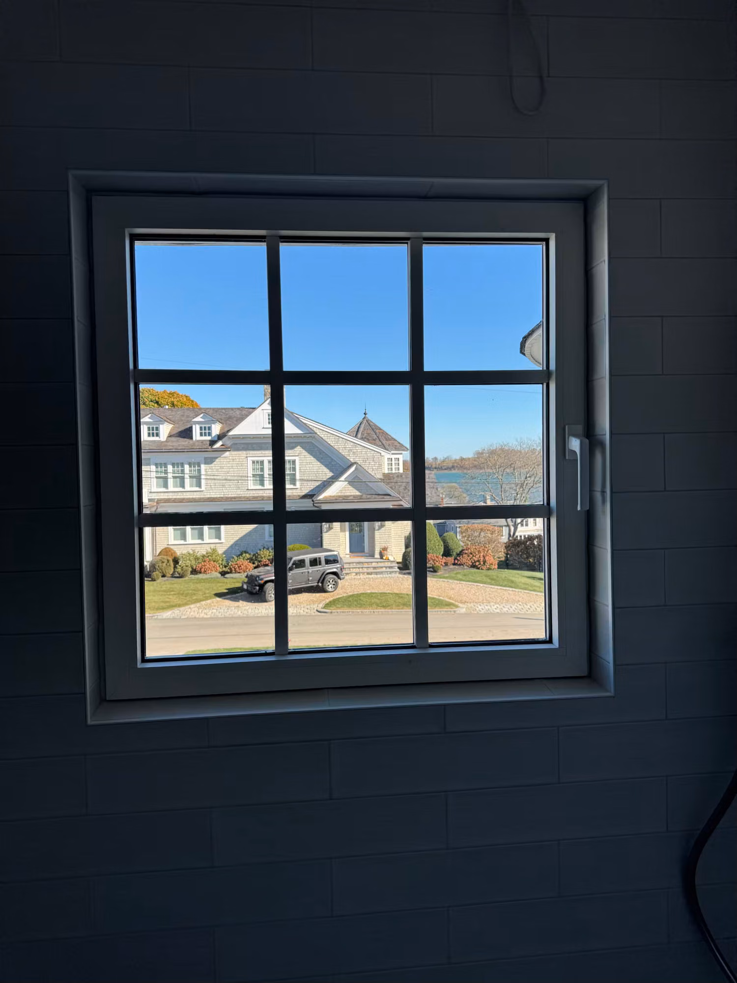 Square divided-light bathroom window set into a dark slate tile wall, overlooking a neighboring home.