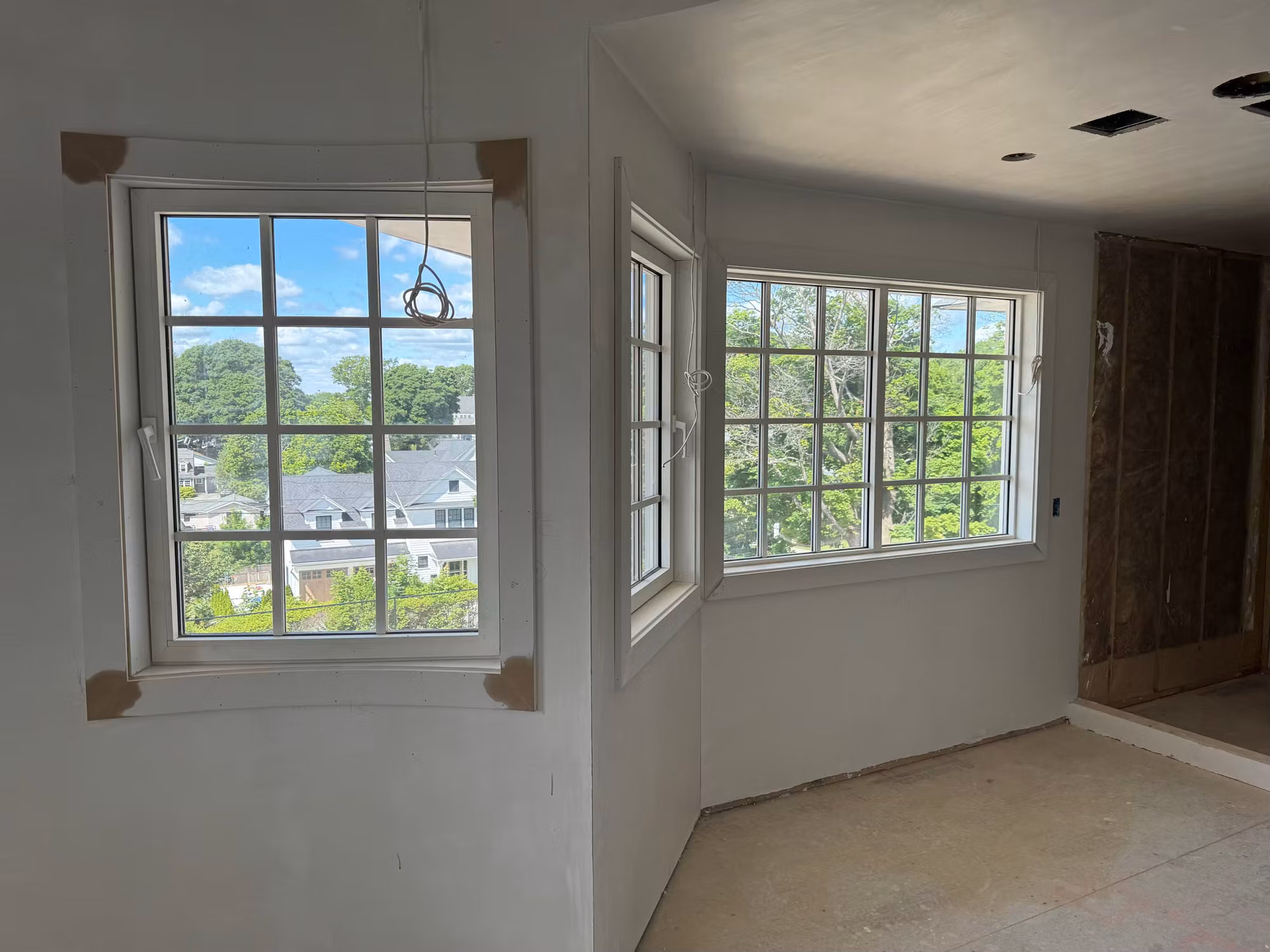 Corner of a room under construction with clear divided-light windows awaiting residential window film.