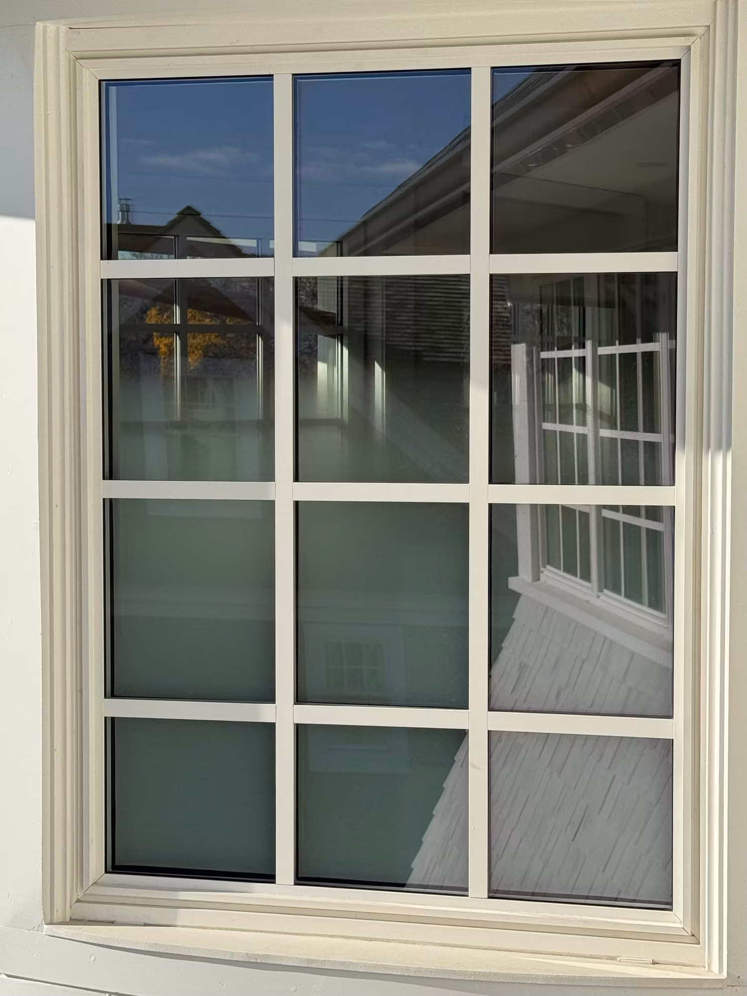 Exterior view of a divided-light grid window showing frosted privacy film diffusing light across the lower panes.