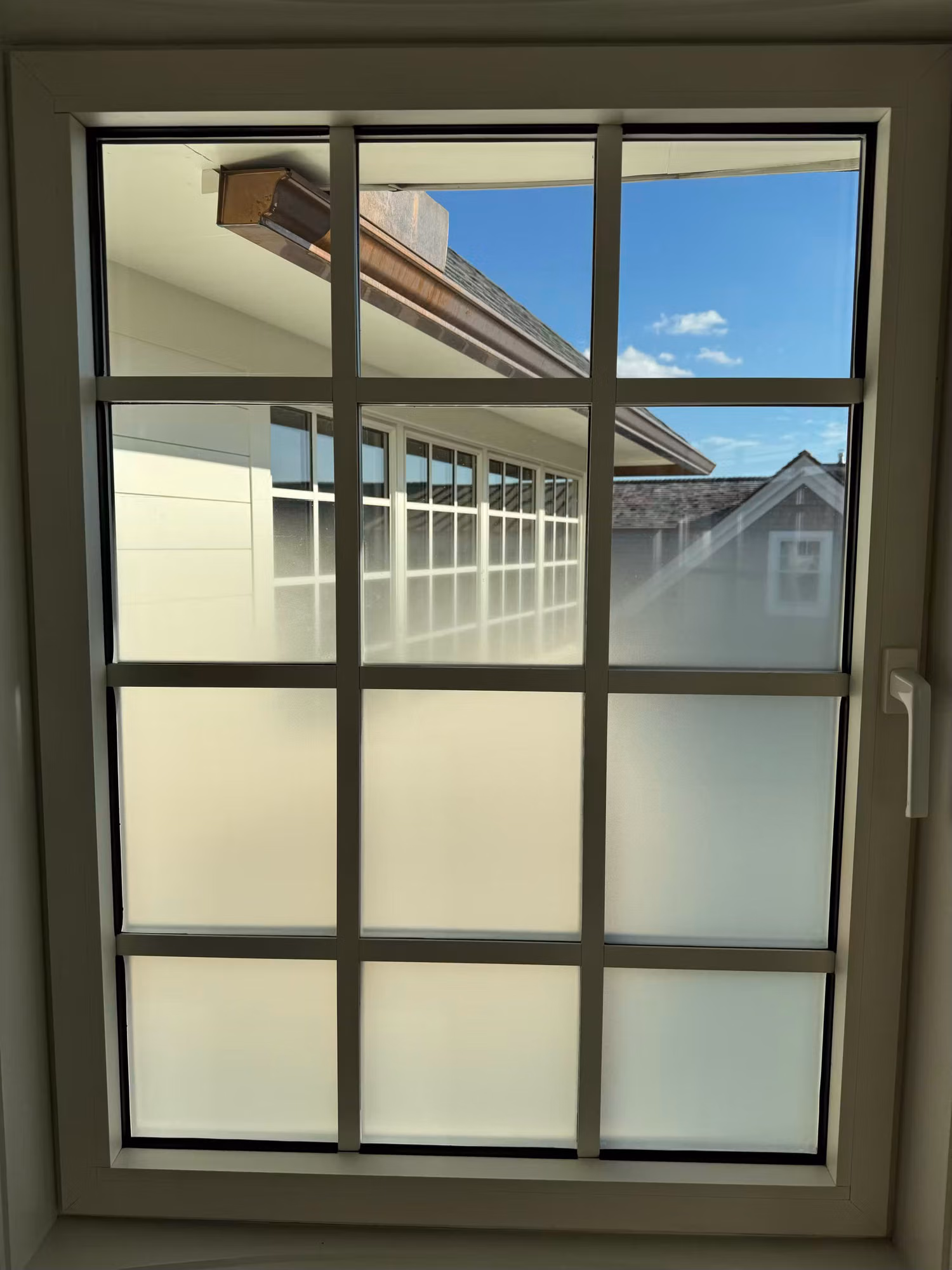 Colonial grid window with frosted privacy film diffusing the lower panes and clear upper panes letting in daylight.