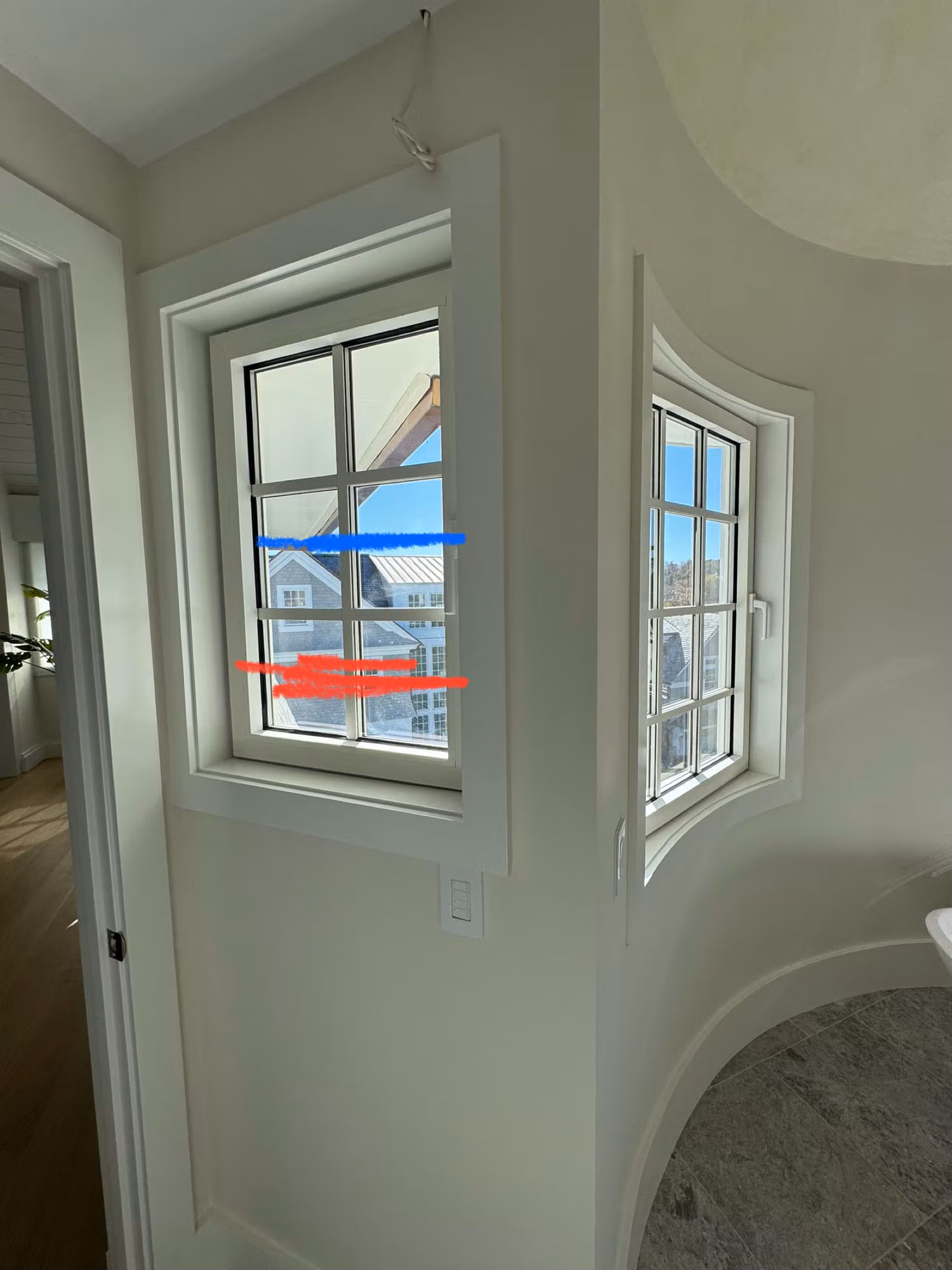 Two corner divided-light windows in a hallway marked with blue and red prep tape during a window film install.