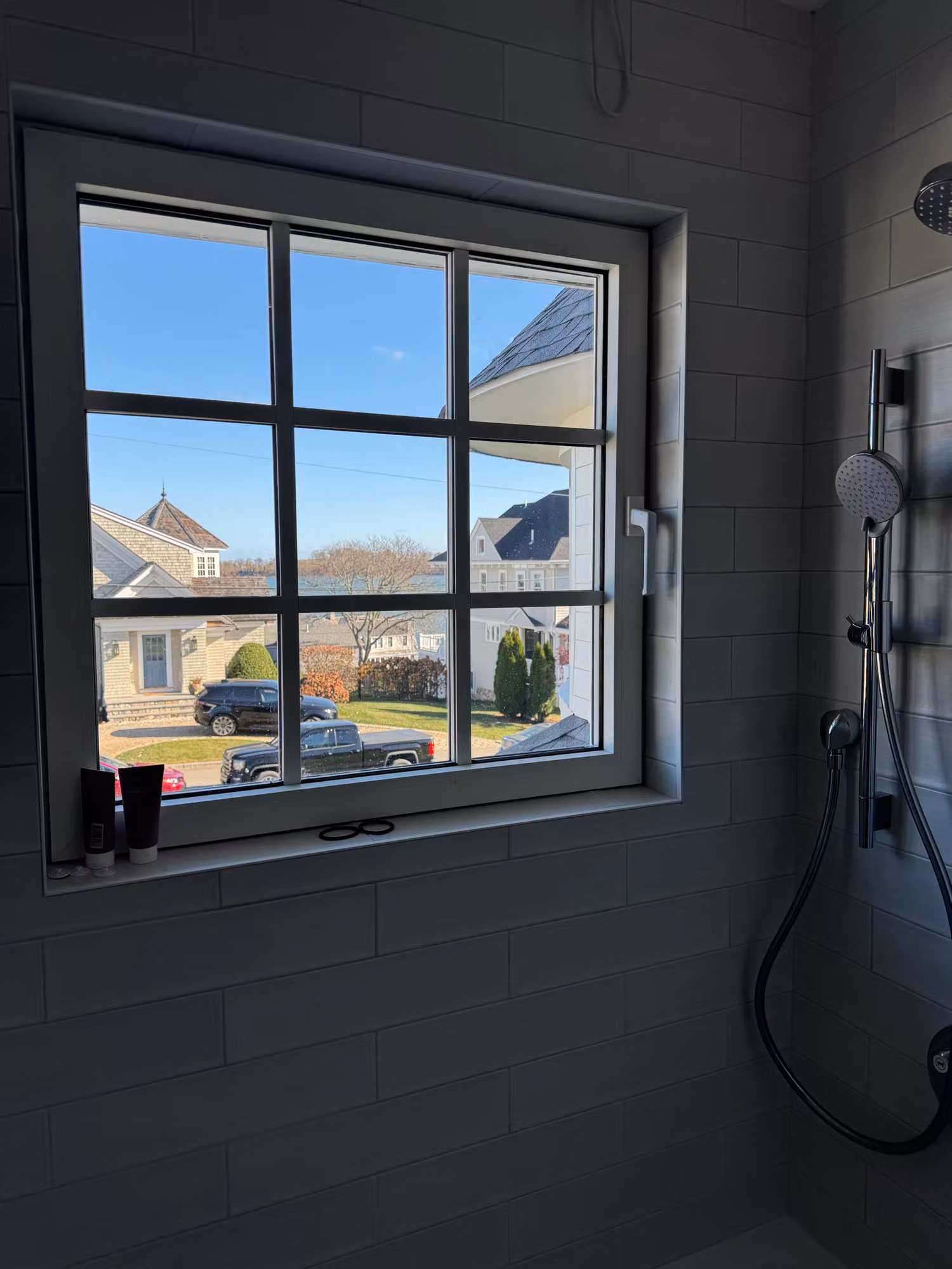 Divided-light window in a tiled walk-in shower with a clear view of the neighborhood beyond.