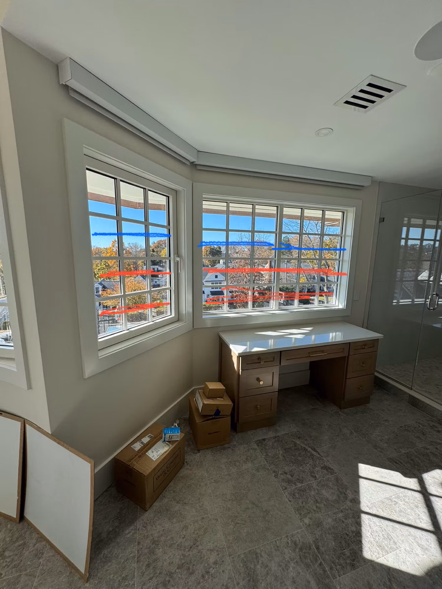 Bay of divided-light windows above a wood desk marked with red lines indicating planned window film areas.