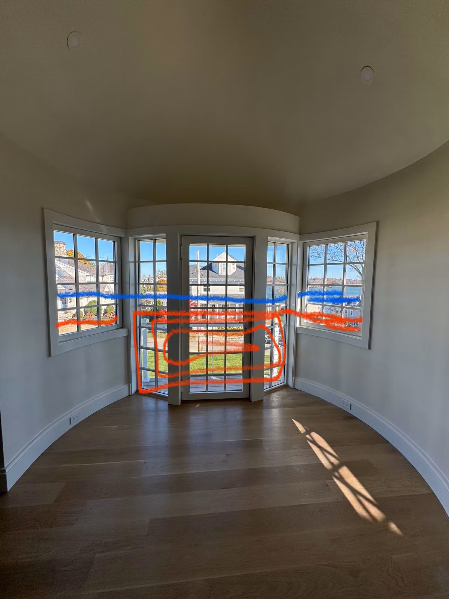 Empty turret room with French-pane glass doors and flanking divided-light windows marked up for window film work.