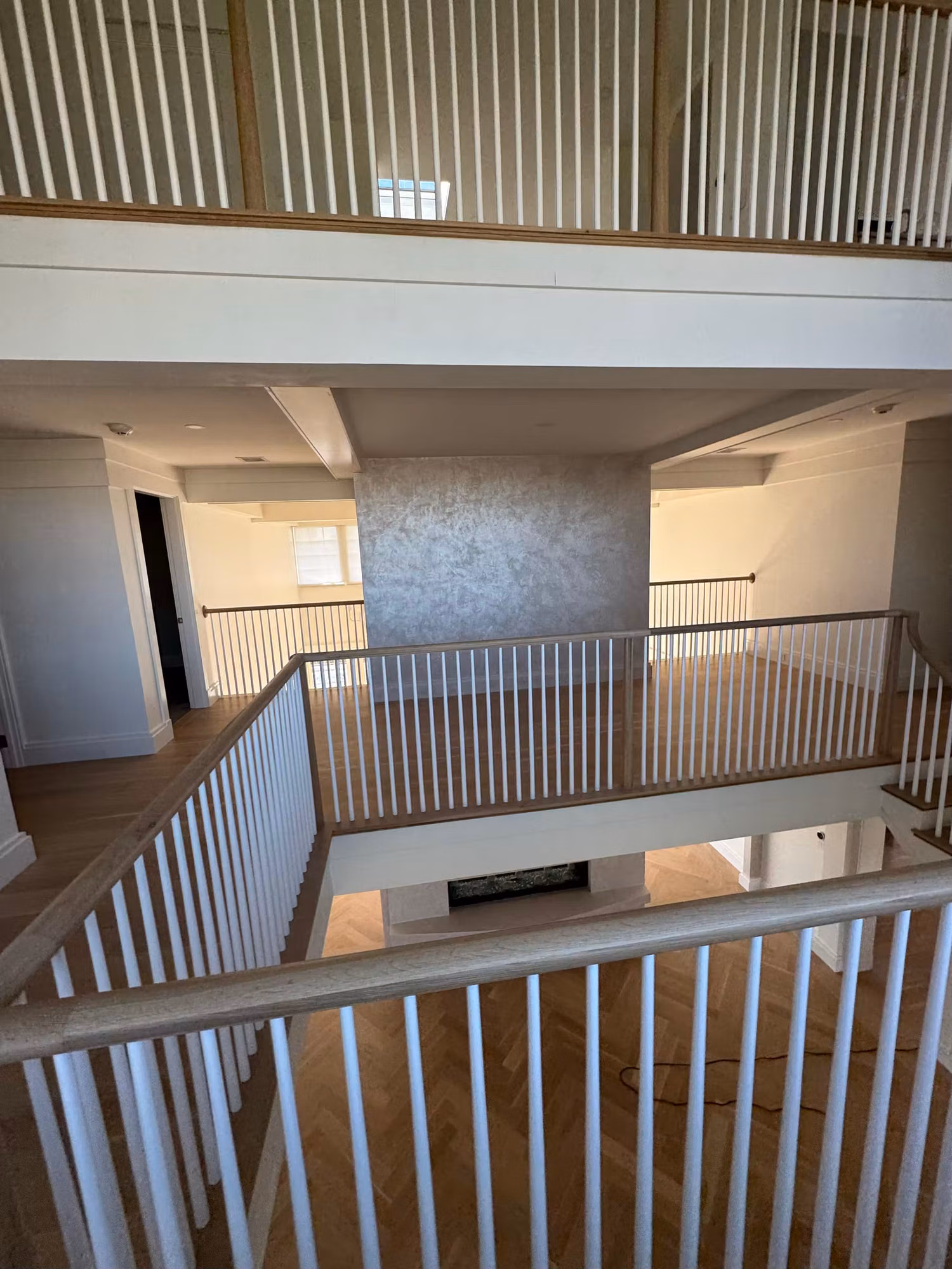 Interior view of a two-story open stairwell landing with white railings and an upper balcony.