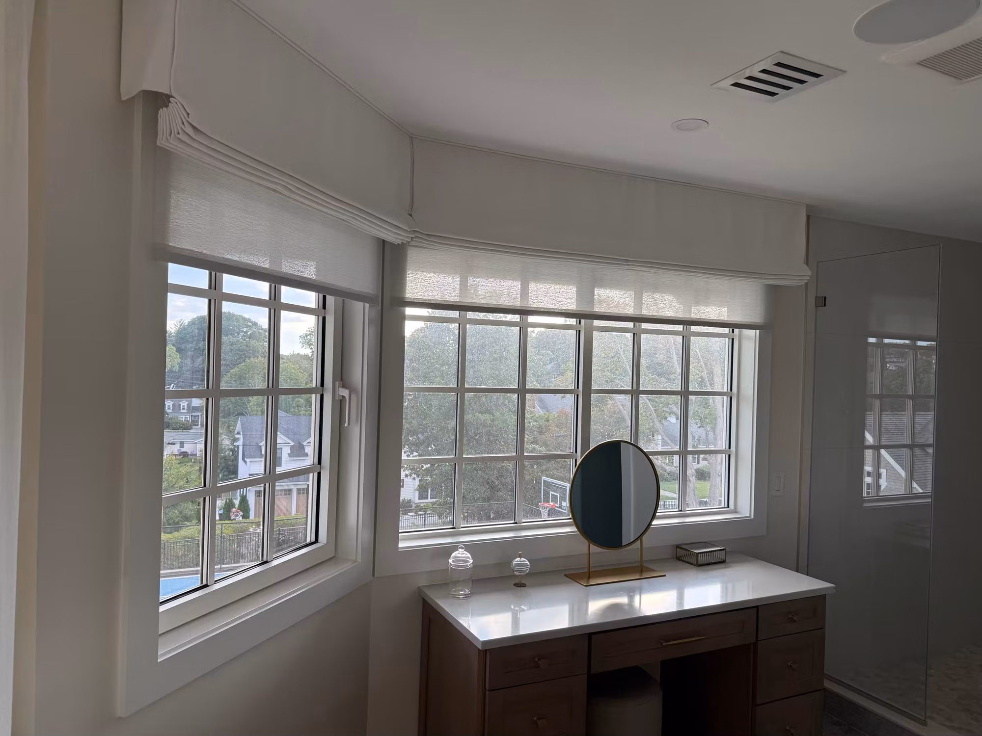 Dressing area with vanity and round mirror beneath grid windows treated with light-diffusing frosted privacy film.