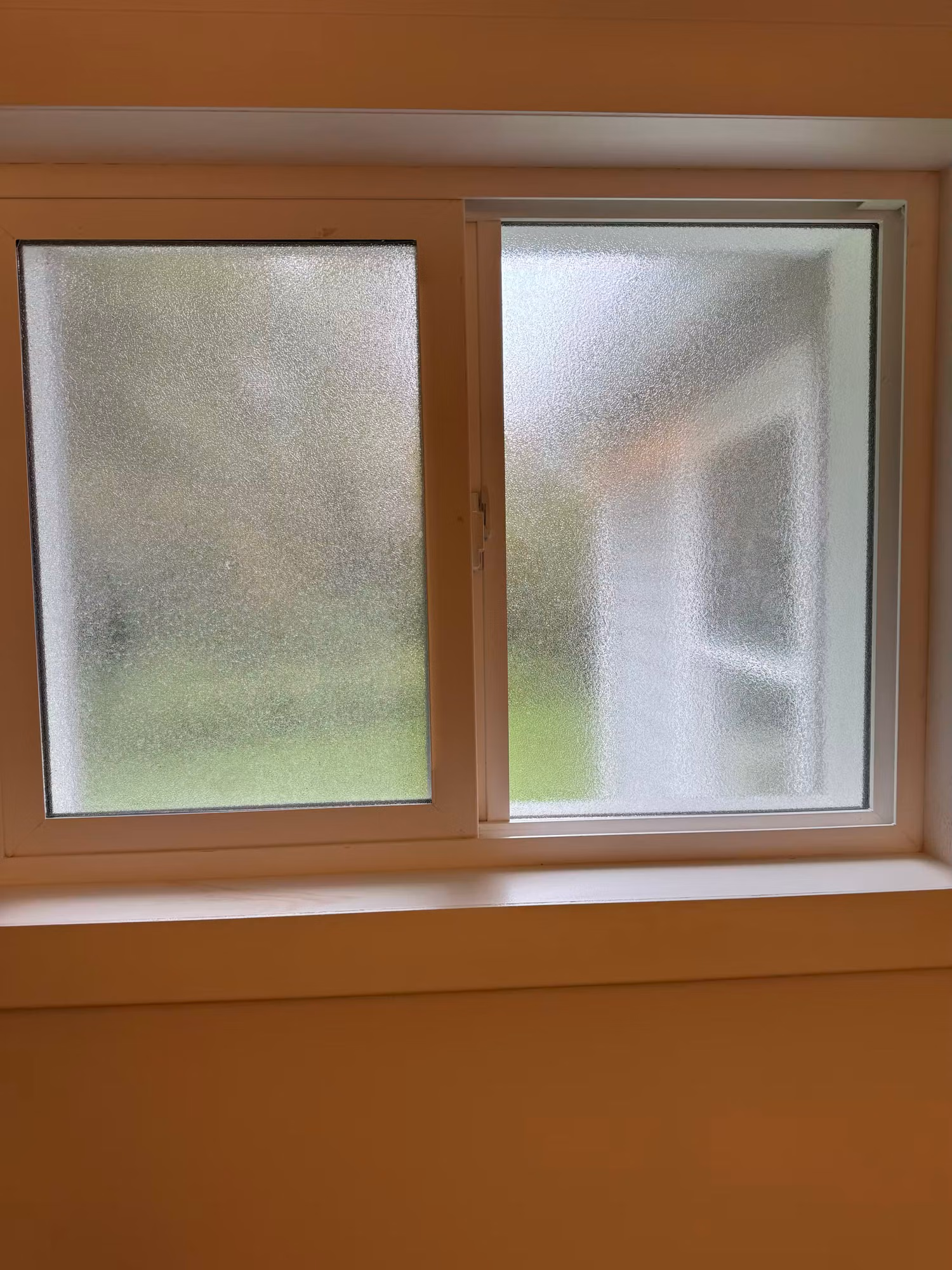 Residential sliding window with frosted privacy film giving a textured ice-like finish that obscures the view while letting in light.