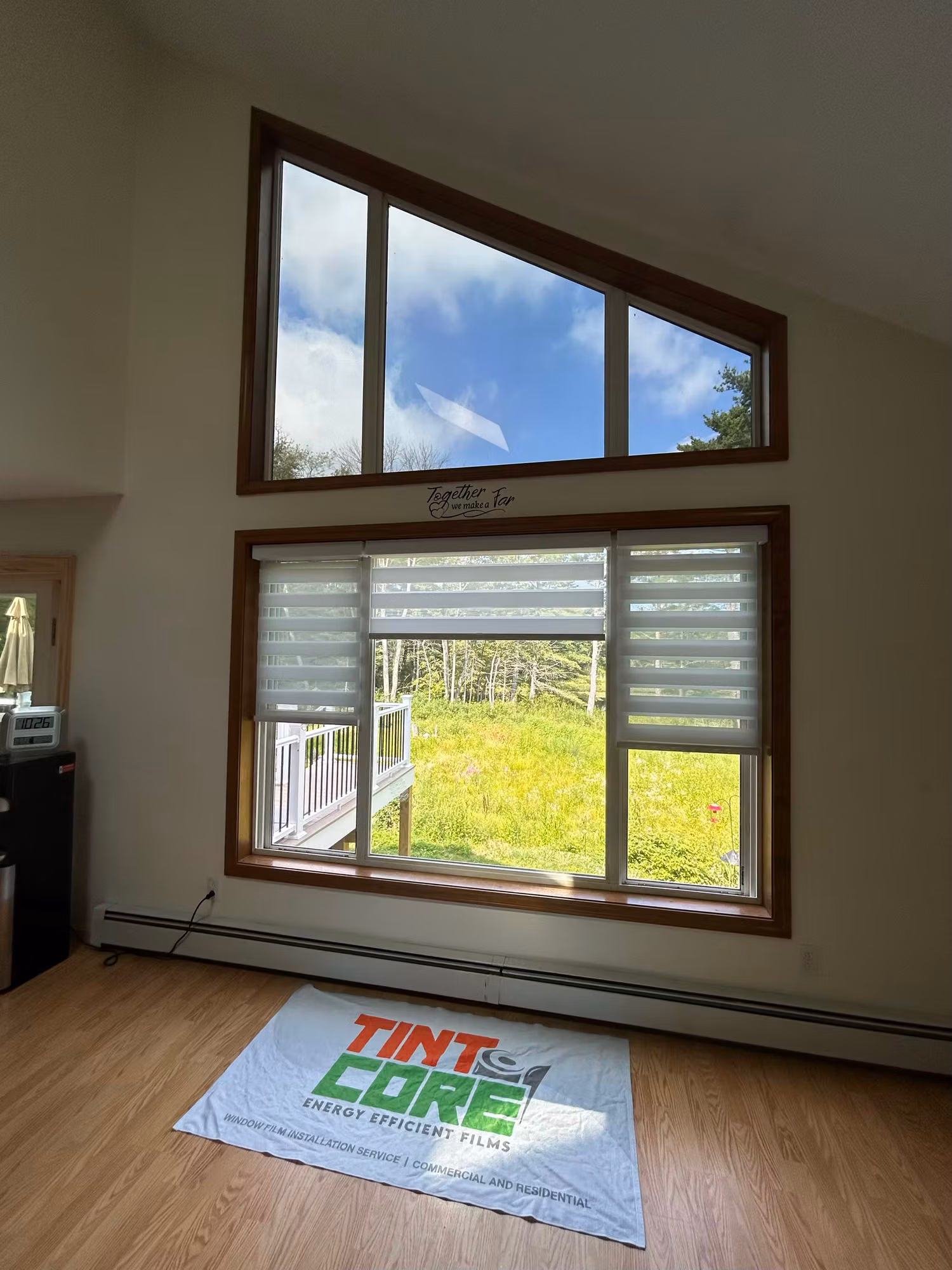 Living room picture window with triangular transom windows above and wood trim, fitted with light-diffusing shades over green field views.