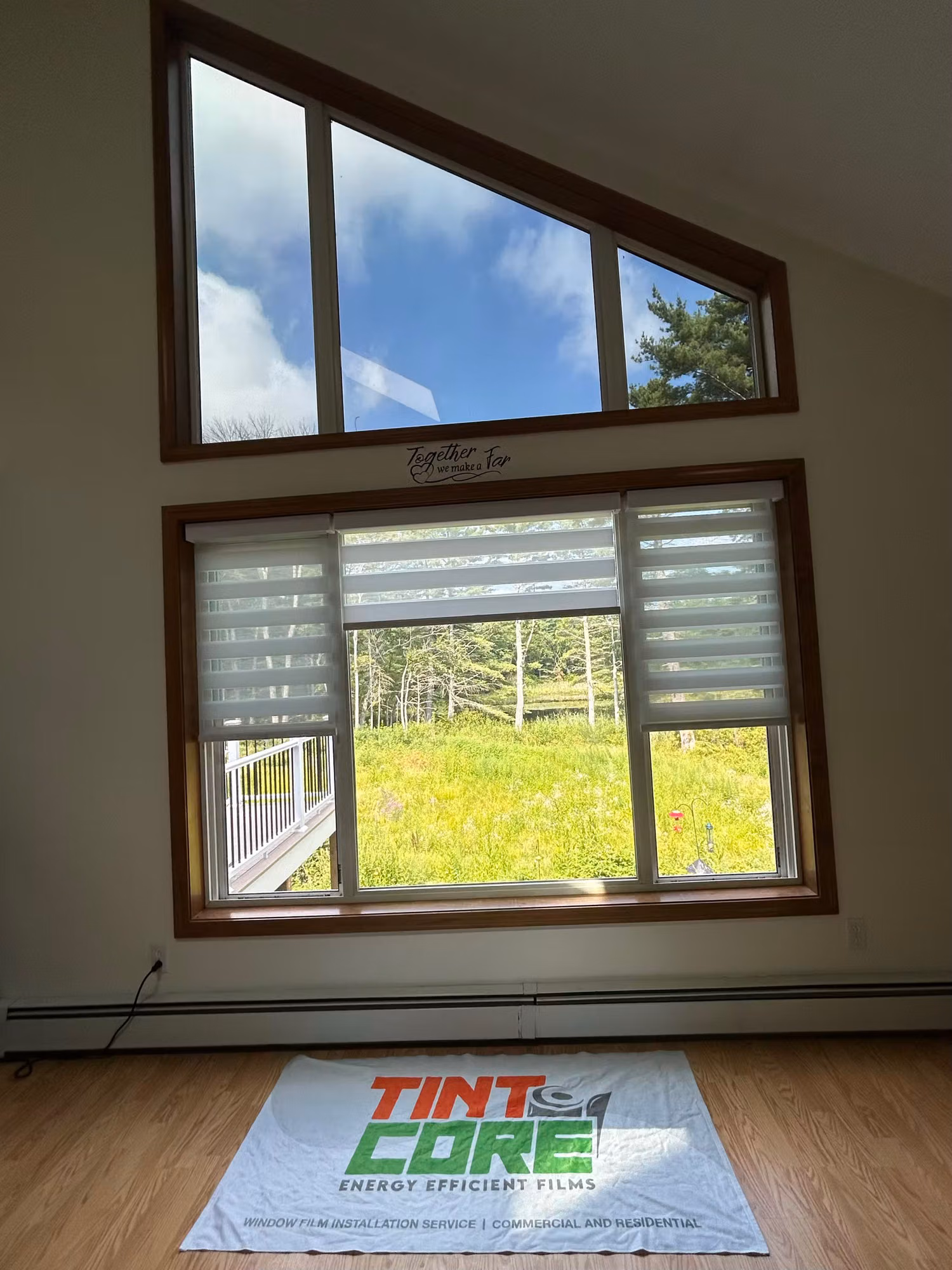 Wood-framed living room picture window with angled transom windows and light-diffusing shades overlooking a grassy backyard.