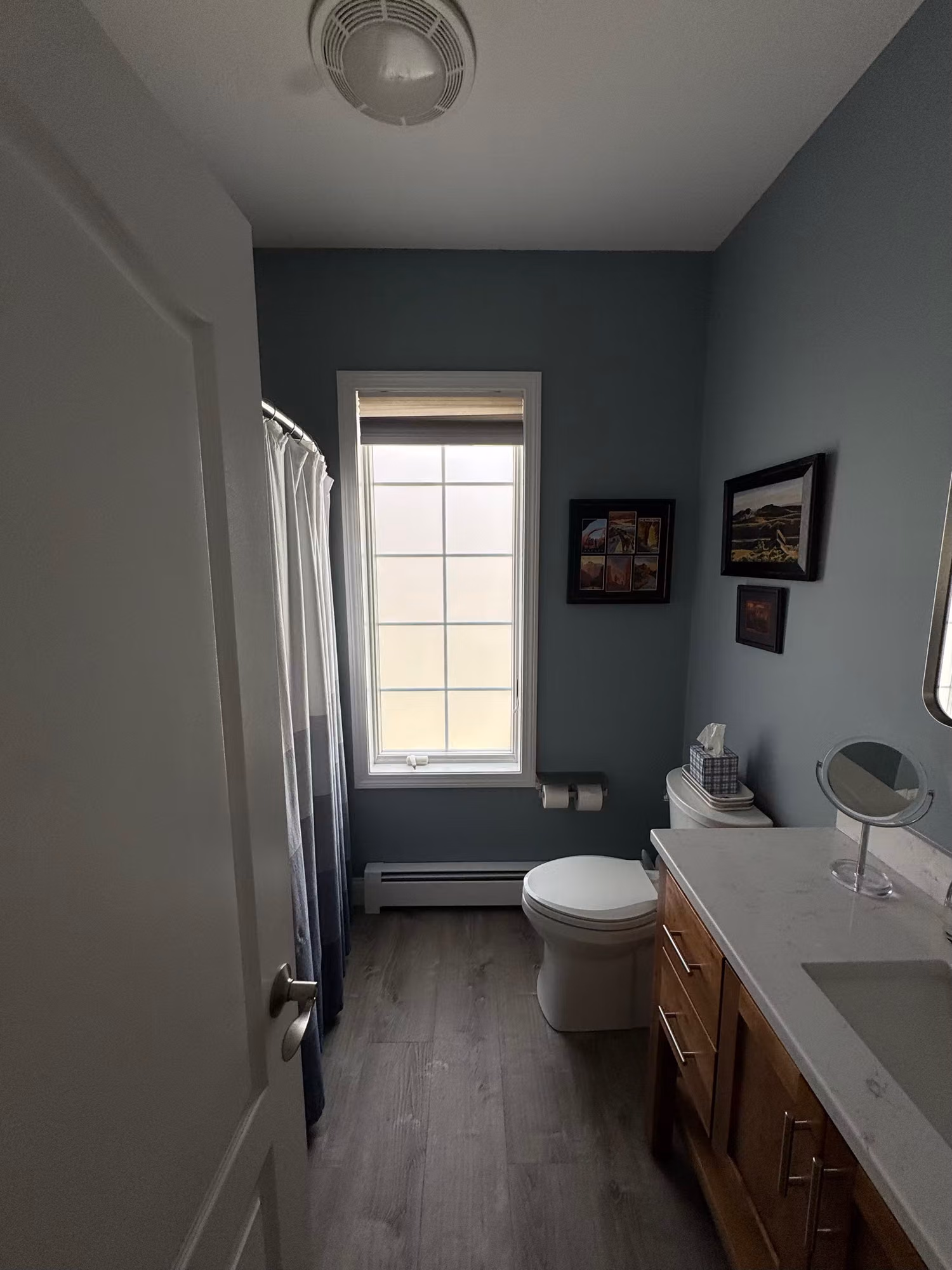 Bathroom window above the toilet set in a vanity and shower area, with a roller shade up and clear glass in soft daylight.