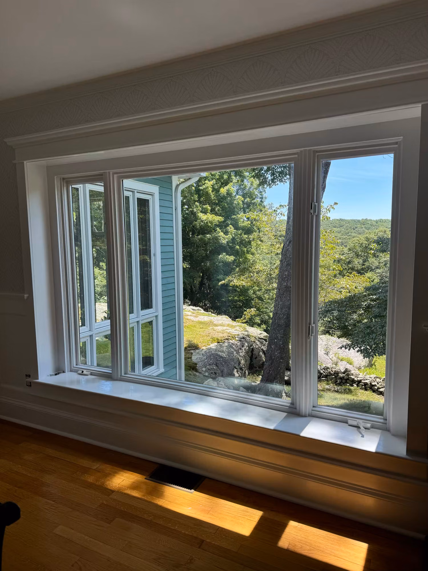 Casement bay window with multiple panes overlooking a hillside and stone wall beyond the glass.