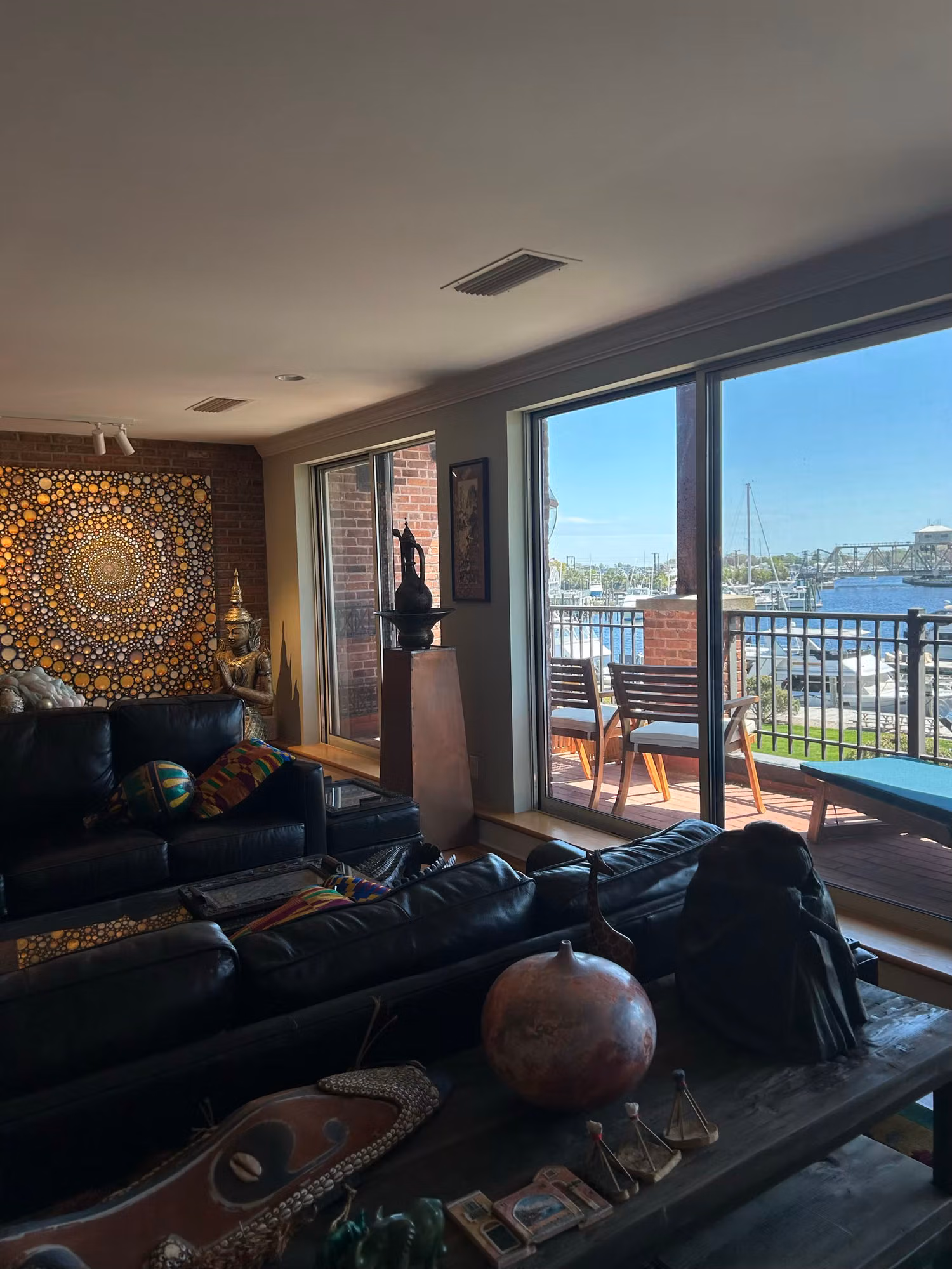 Sunlit living room with a sliding glass balcony door framing a marina view, leather seating inside.