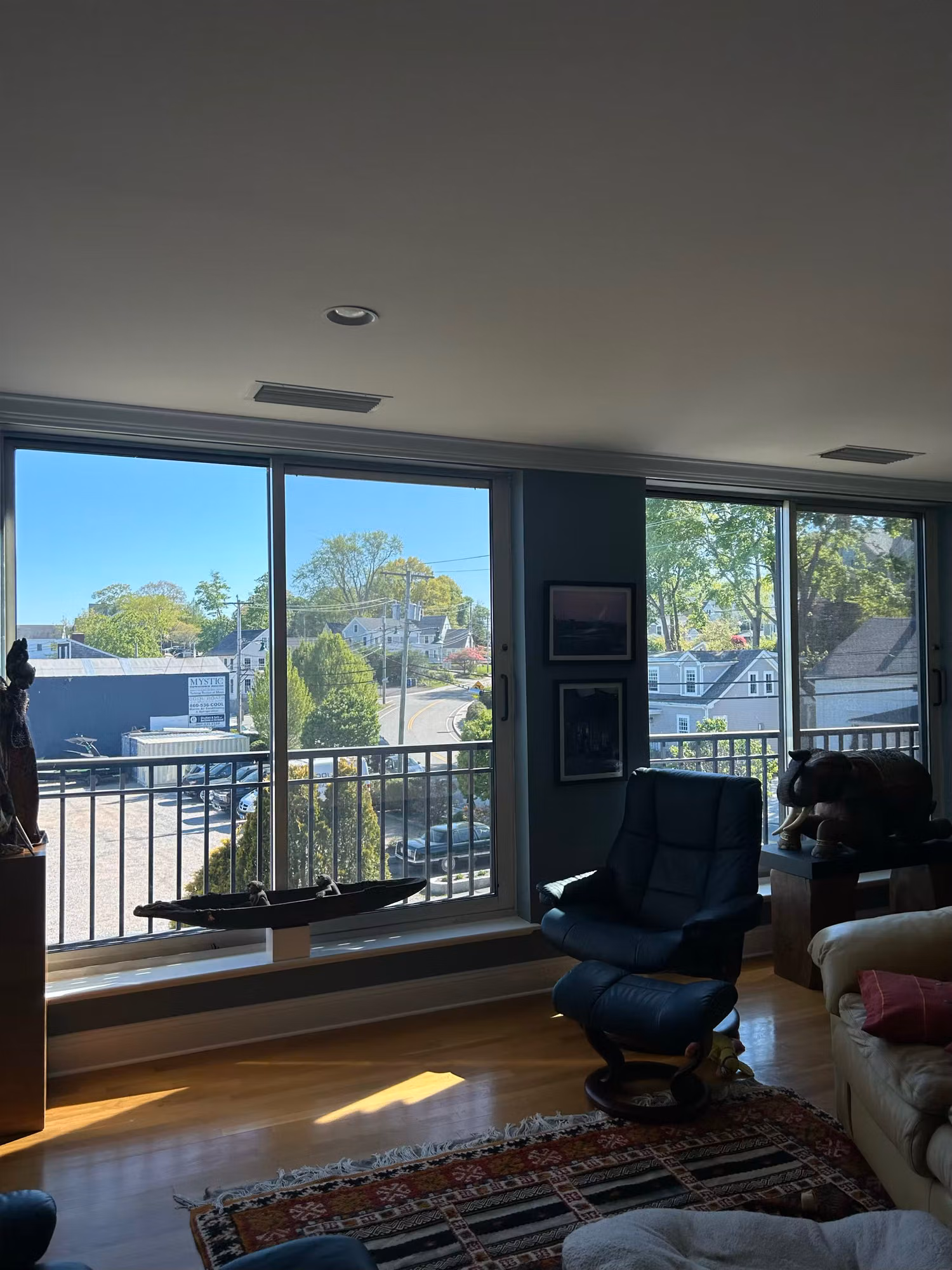 Living room corner with large windows and a recliner facing a bright sunlit outdoor view.