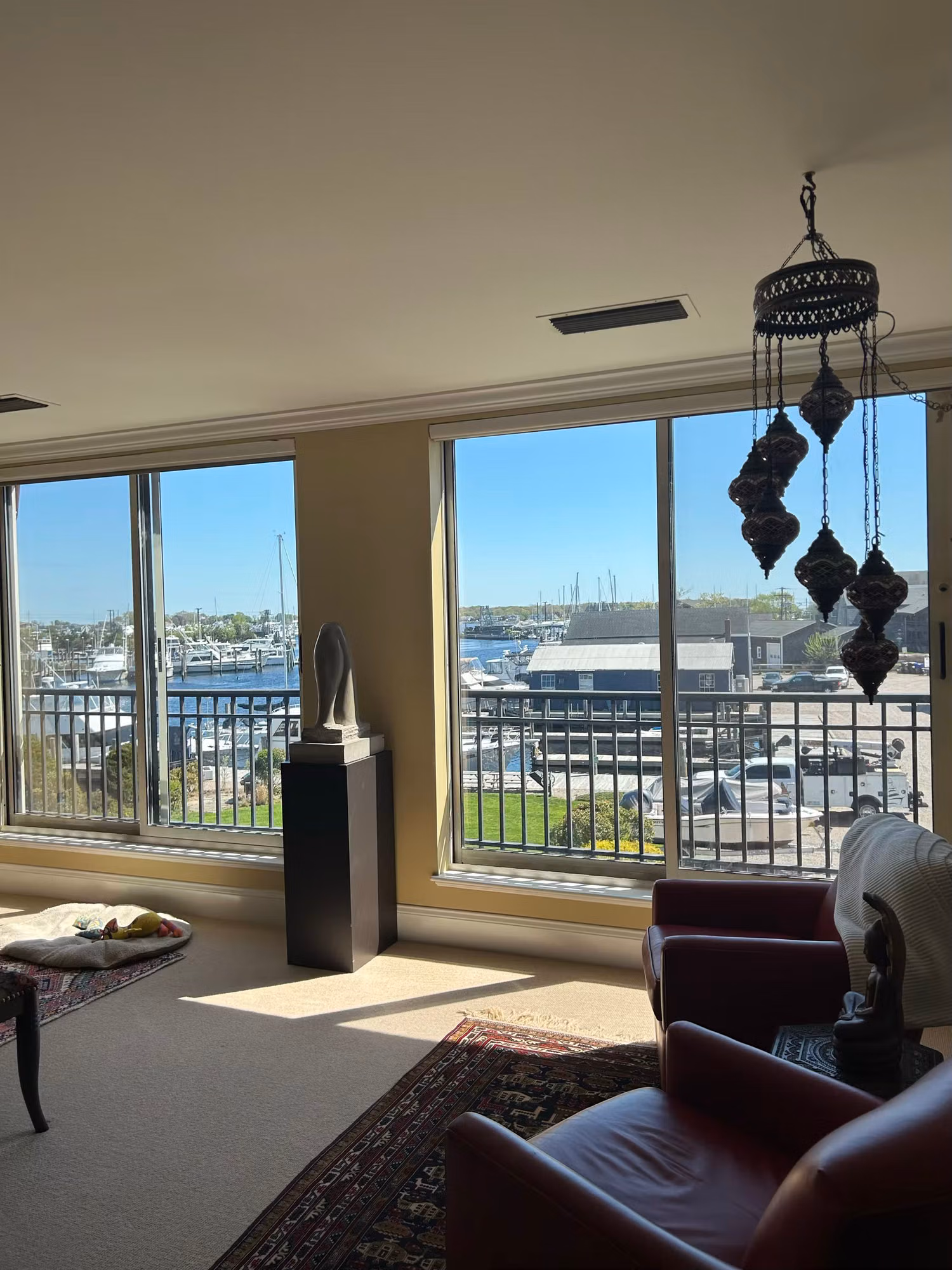 Bright living room corner with two large picture windows looking out over a sunny marina.
