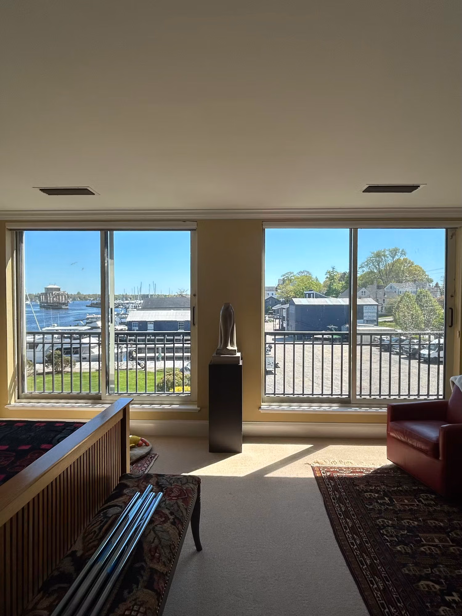 Furnished living room with two tall picture windows overlooking a bright waterfront marina.