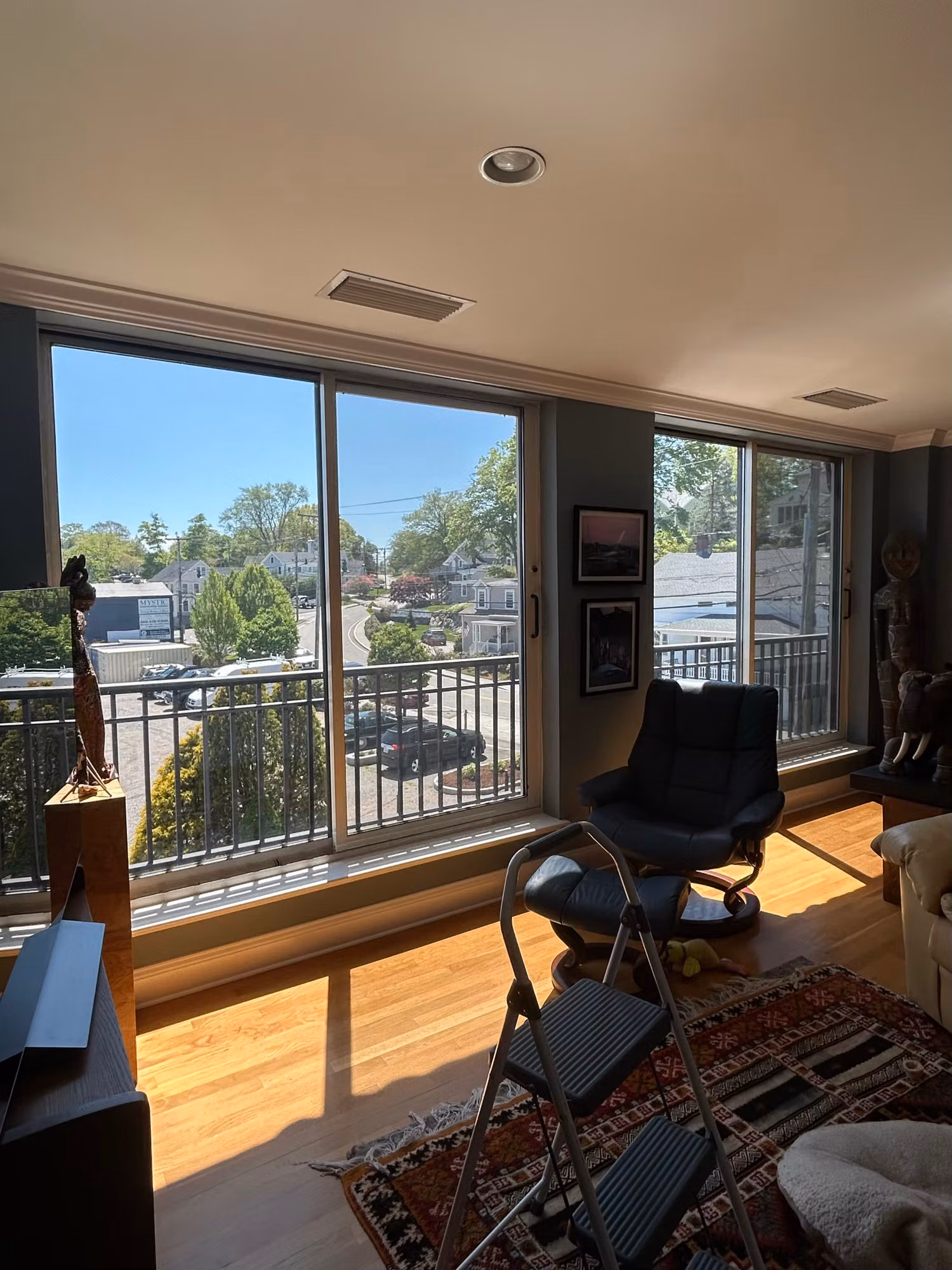 Bright living room with large sliding glass doors to a balcony and a sunlit rooftop town view, glass treated with film.