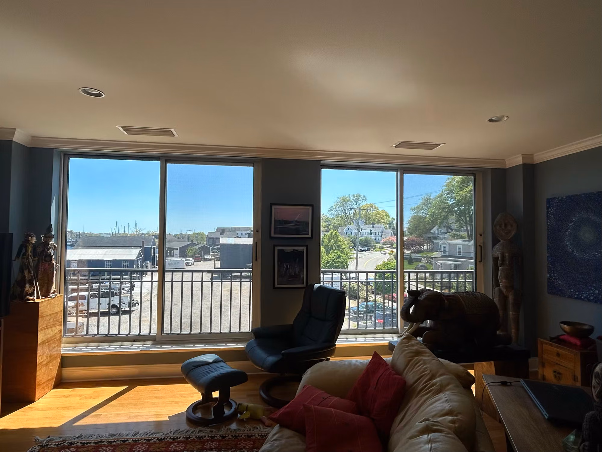 Living room with two large sliding glass doors to a balcony, treated glass framing a sunny harbor and town view.