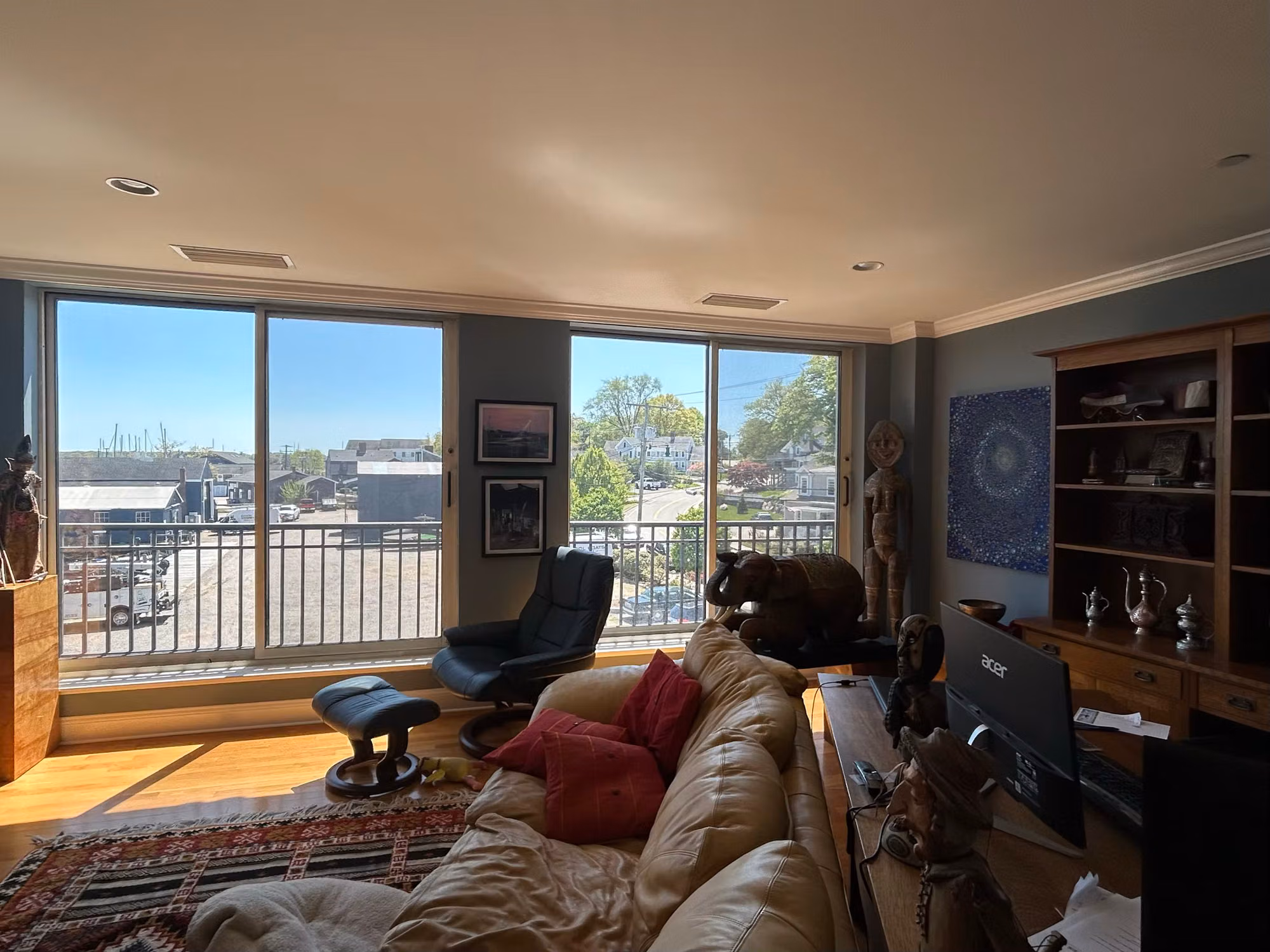 Sunlit living room with two large sliding glass doors and a balcony, treated glass over a rooftop and harbor view.