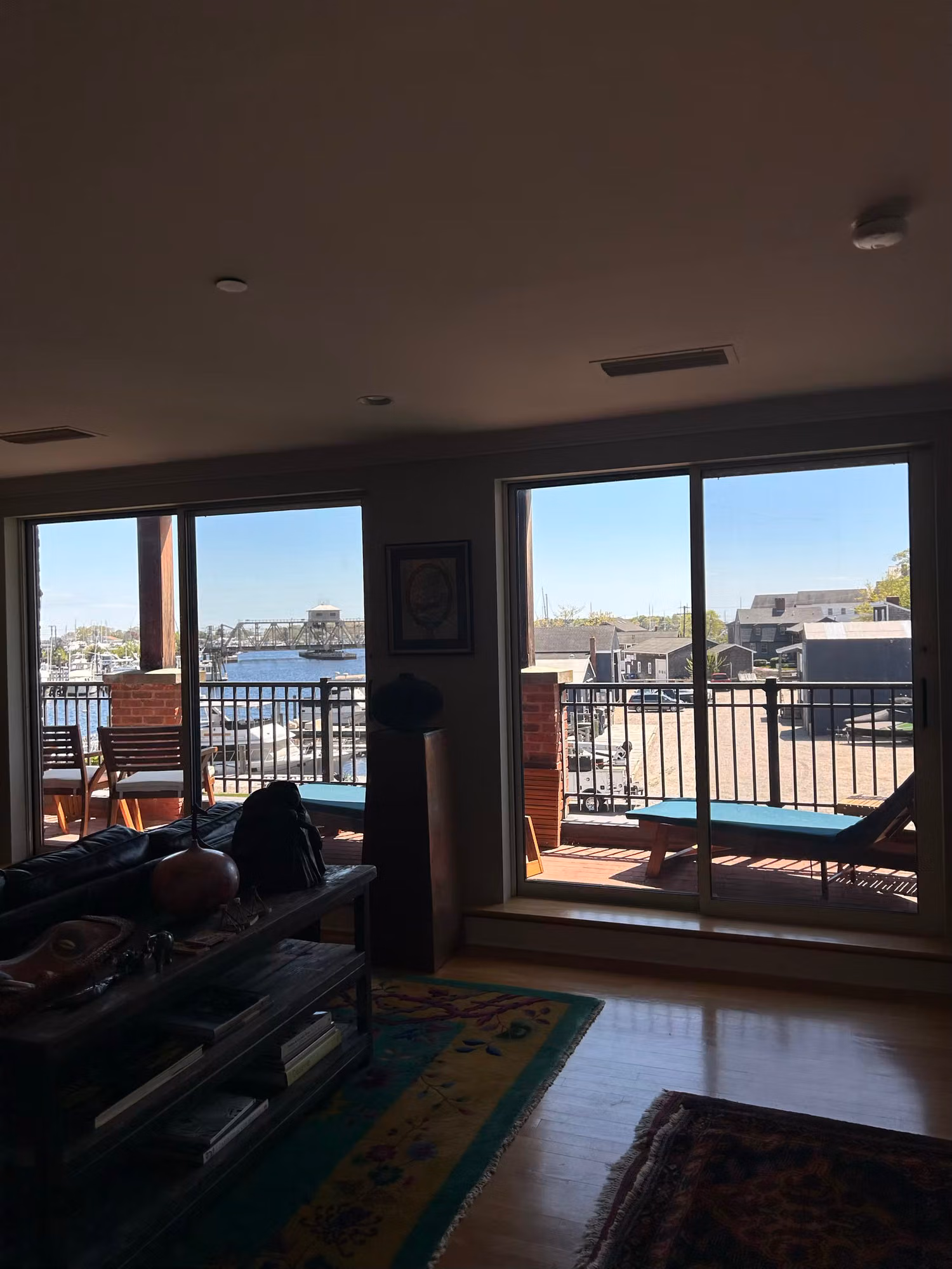 Living room with large sliding glass doors opening to a balcony and a bright waterfront harbor view, glass treated with film.