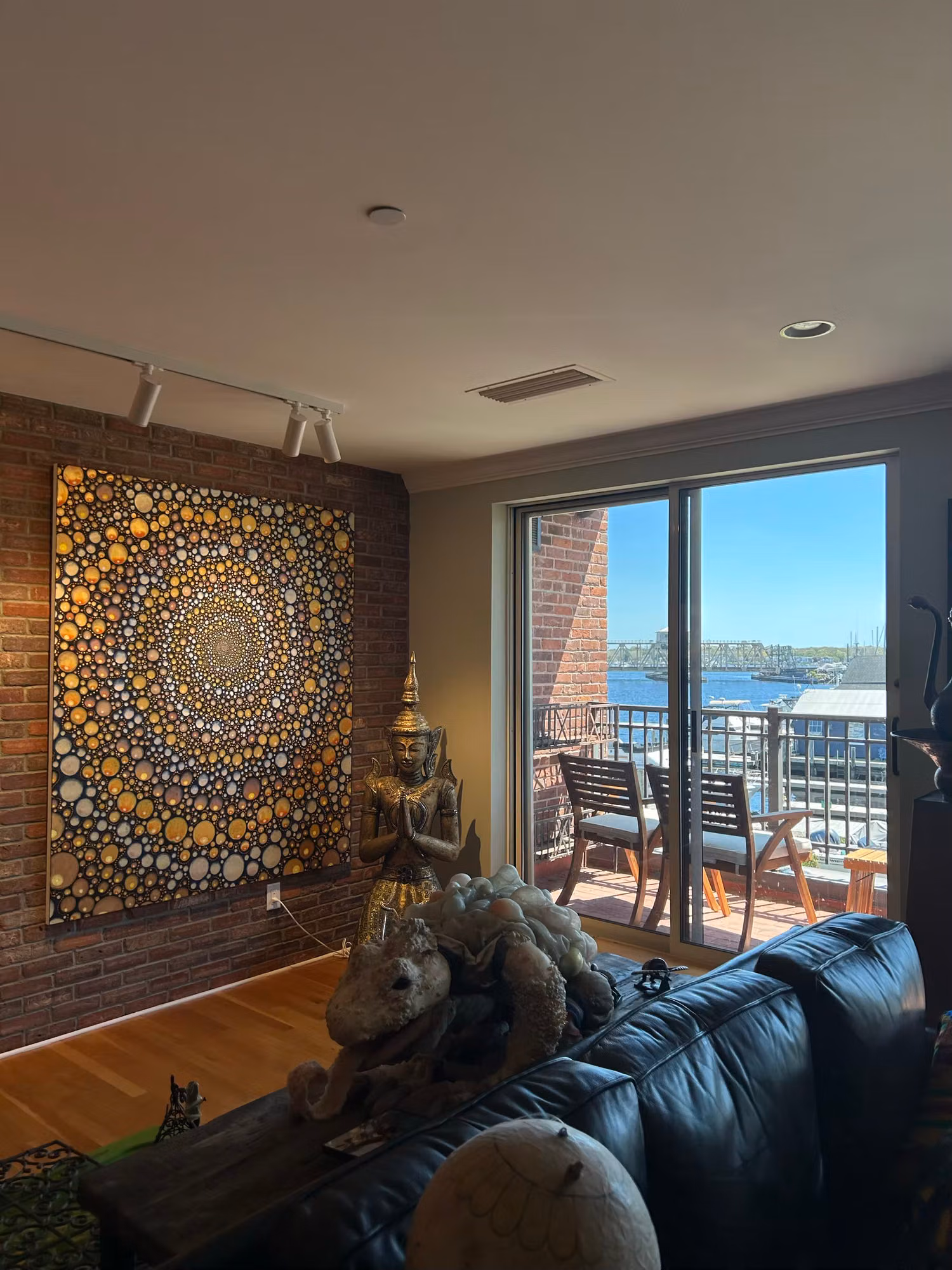 Living room with exposed brick and a sliding glass door to a balcony over a sunny harbor, glass treated with film.