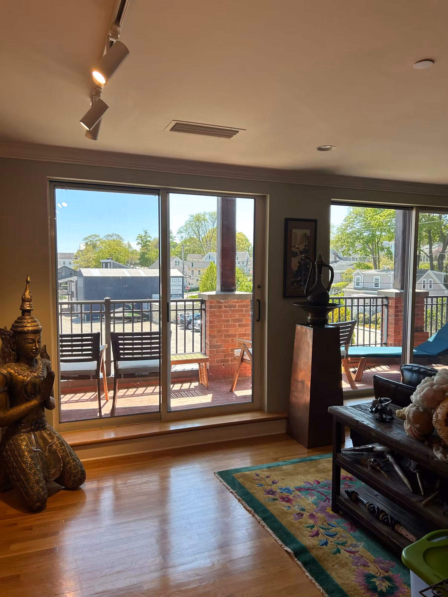 Bright living room with large sliding glass doors and a balcony framing a sunlit town view, glass treated with film.