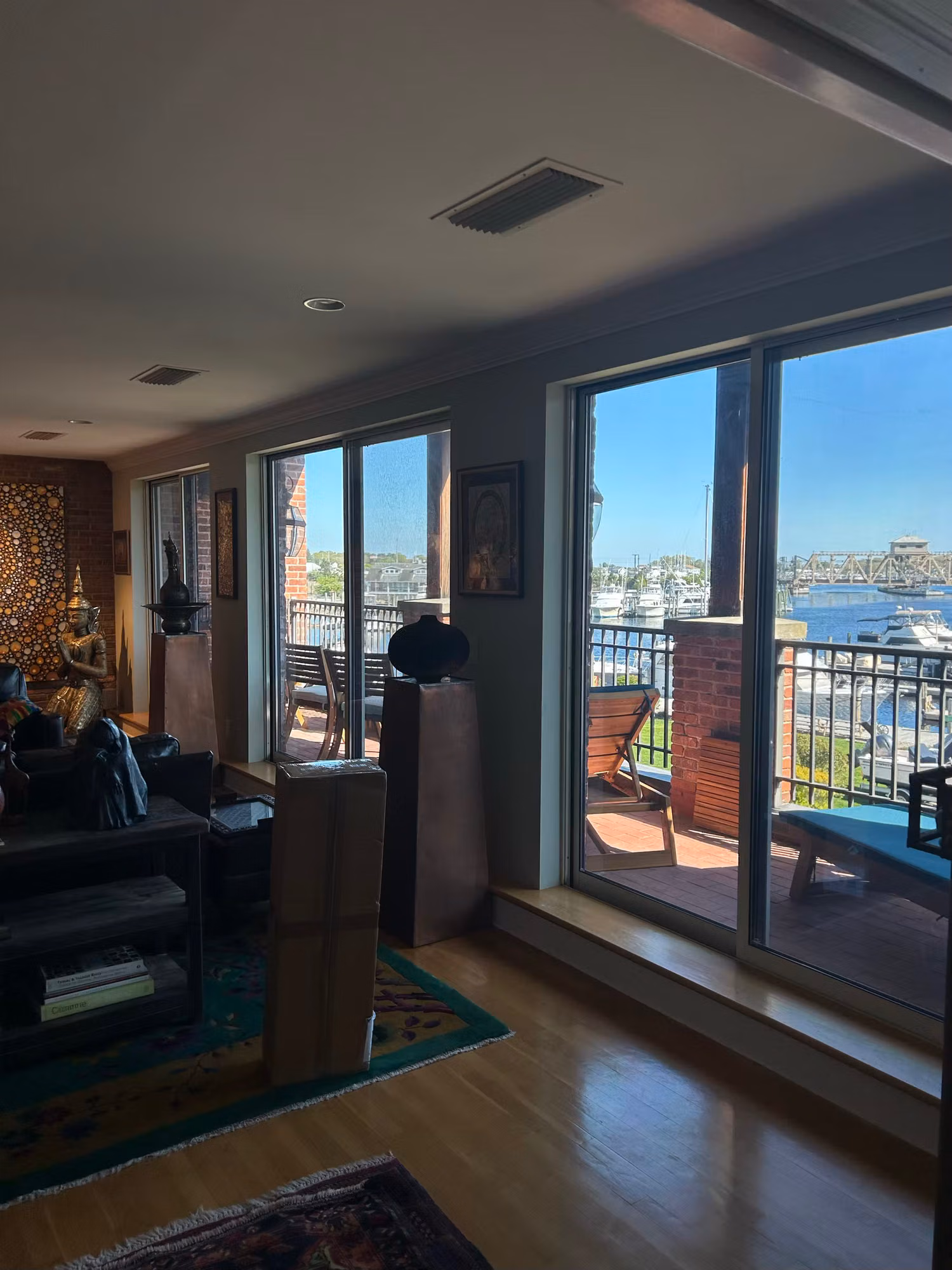 Living room with sliding glass balcony doors overlooking a sunlit harbor, furnishings inside.