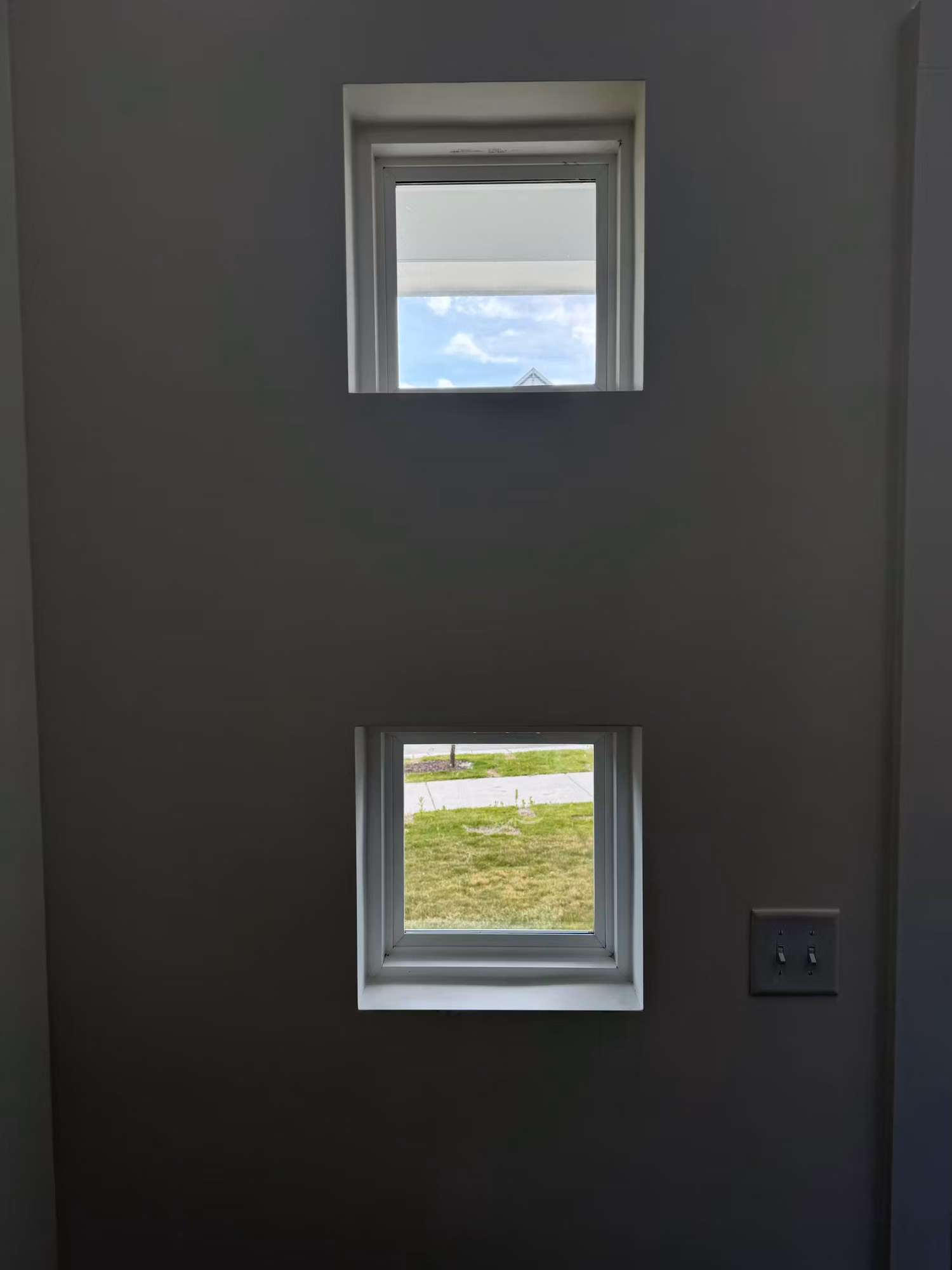 Two small square windows set into a dark accent wall, looking out to a green lawn and bright sky.