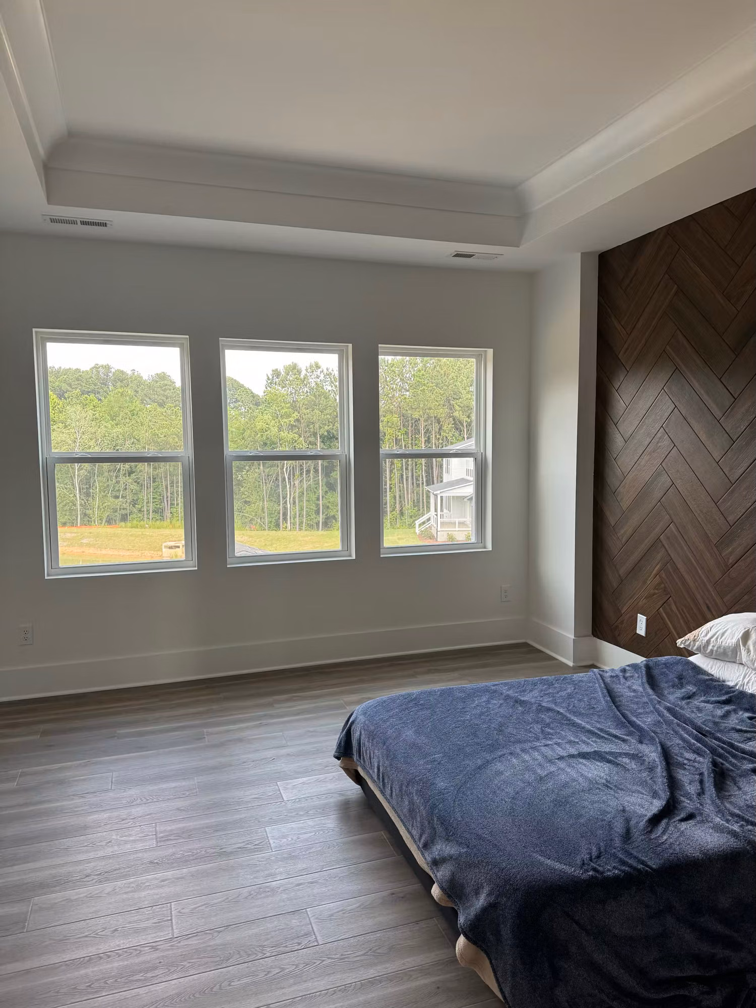 Three bedroom picture windows fitted with window film overlooking a wooded backyard beside a herringbone accent wall.
