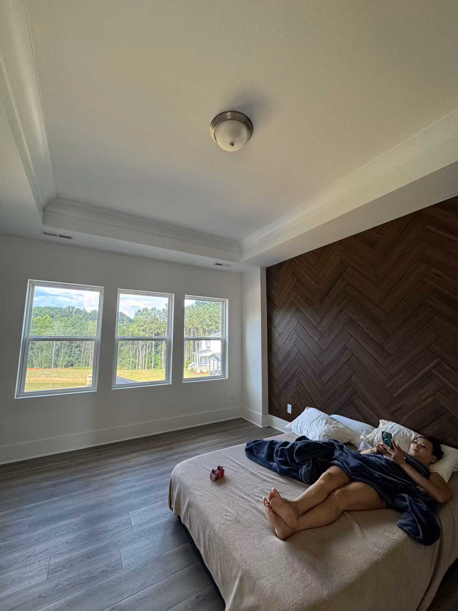 Three bedroom windows with clear residential film framing a treeline view beside a herringbone accent wall.
