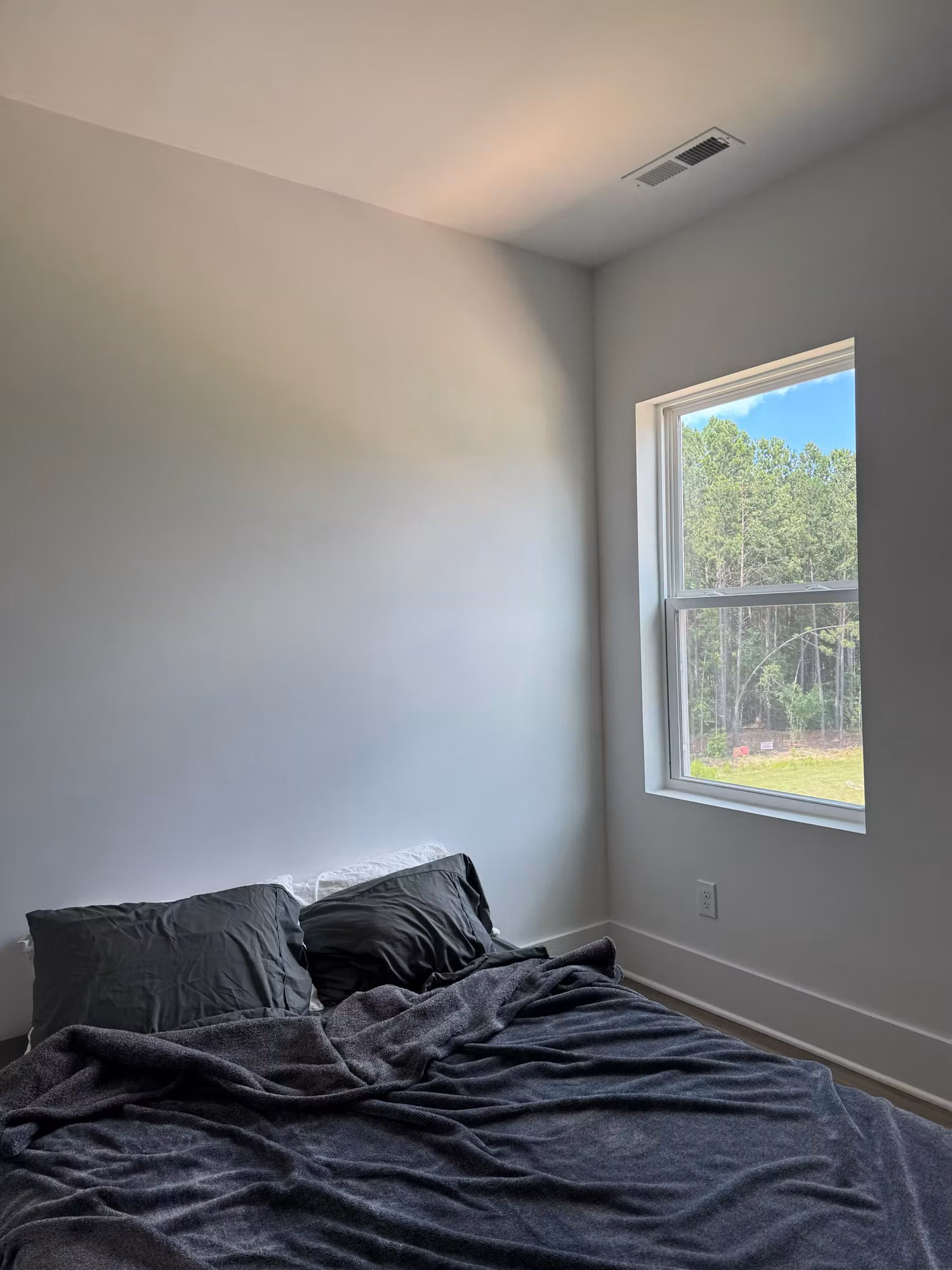 Small bedroom with a single tinted window letting in light over a bed, with treeline visible outside.