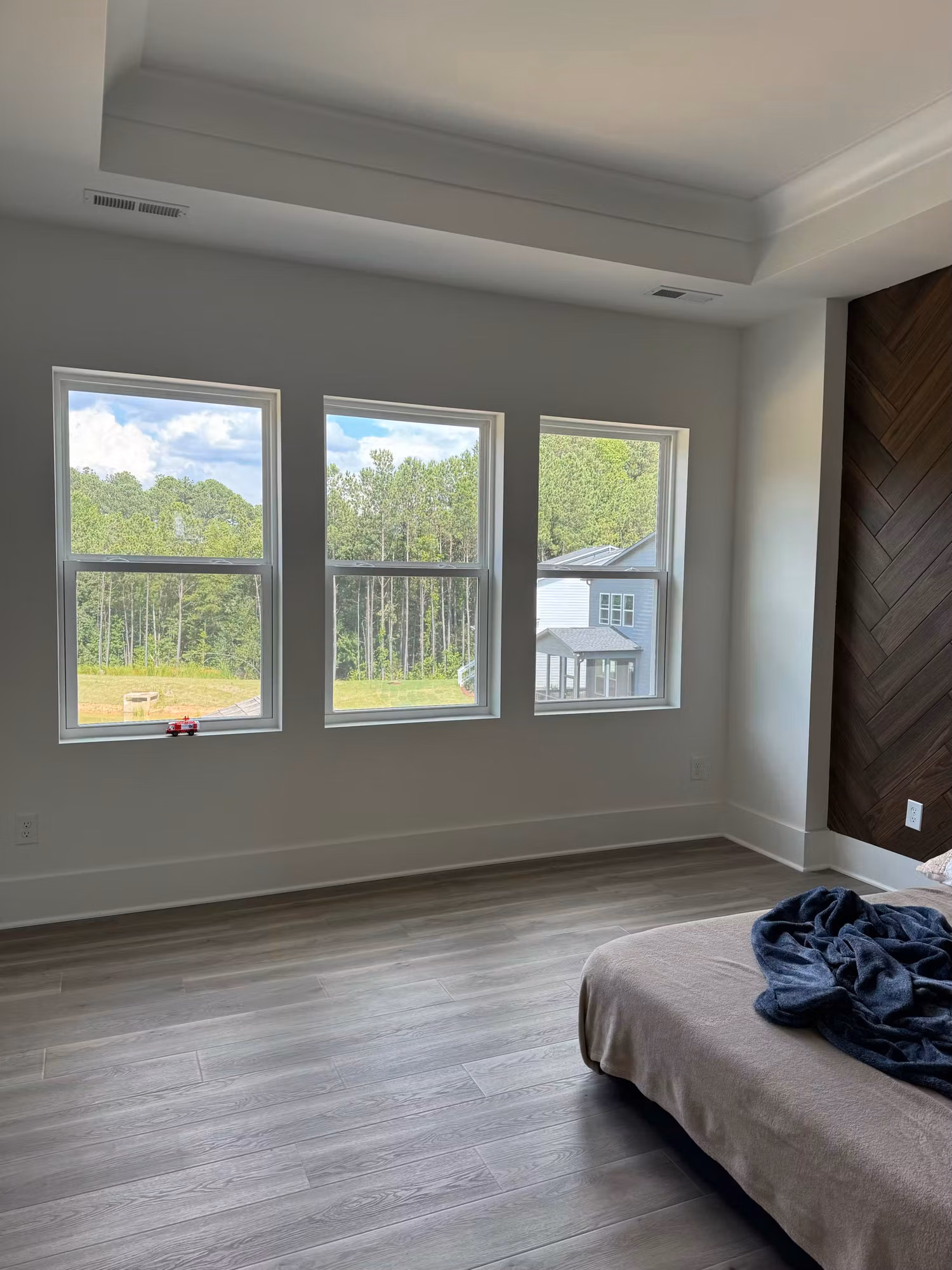 Three bedroom windows with window film in a tray-ceiling room looking out to trees and a neighboring home.
